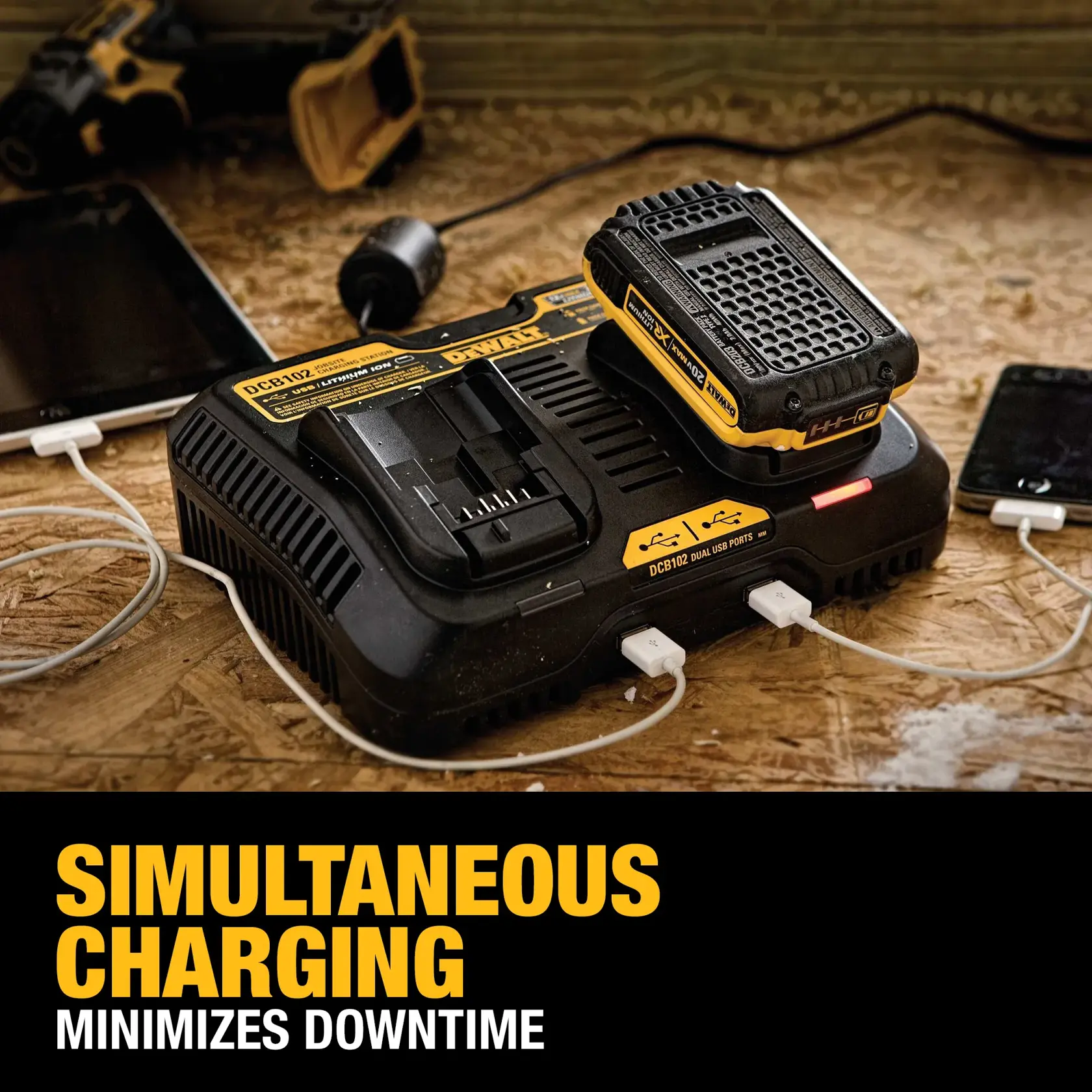 DEWALT DCB102 dual battery charger on a workbench, charging a power tool battery and two mobile devices via USB ports. Text on image reads 'Simultaneous Charging Minimizes Downtime.'