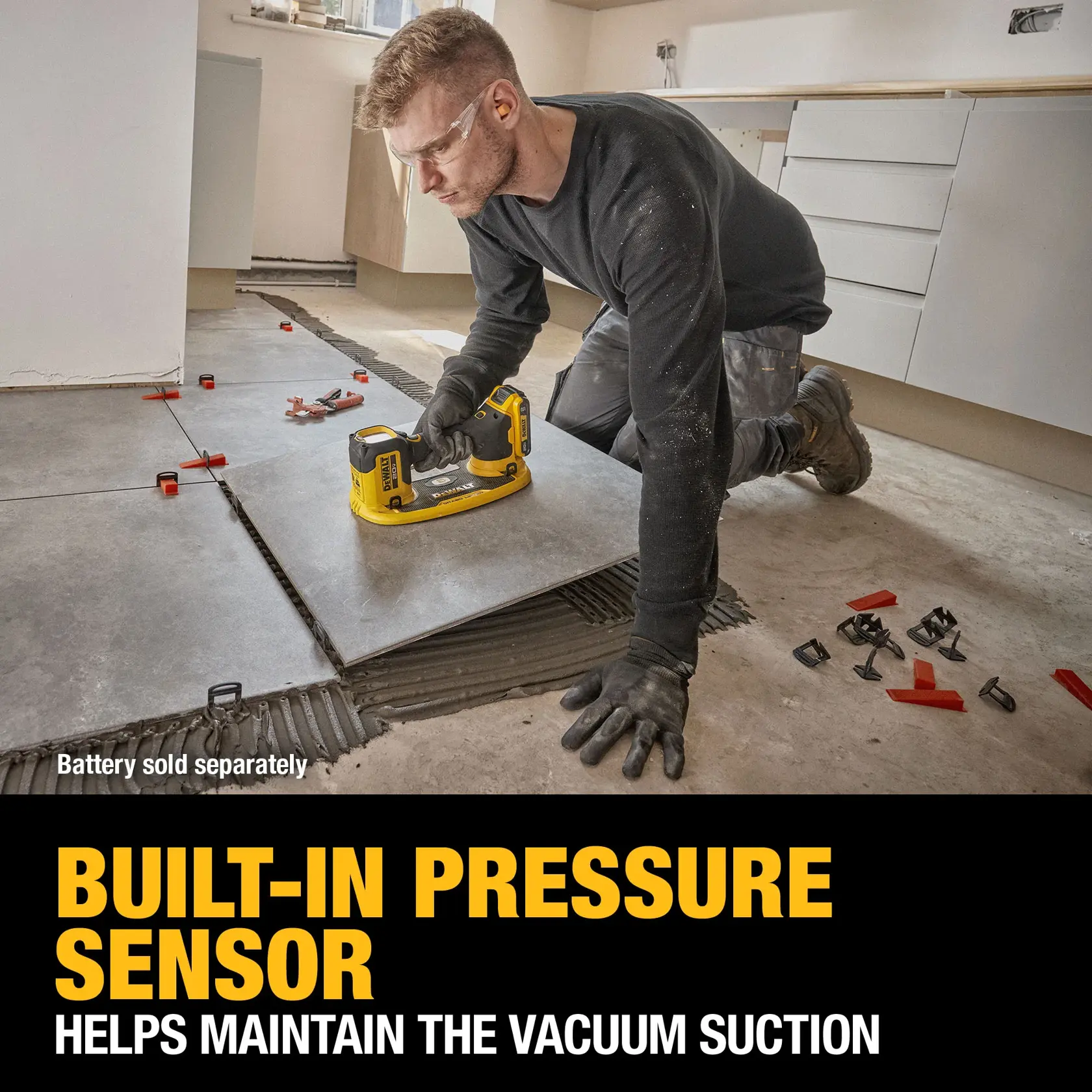A person wearing gloves is installing large floor tiles in a kitchen using a DEWALT vacuum suction tool with a built-in pressure sensor. Various tile spacers and clips are scattered nearby. The text overlay highlights the tool’s built-in pressure sensor feature. The person's face is blurred. Battery is sold separately.