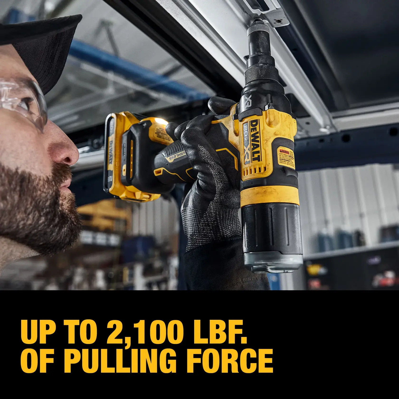 A gloved person uses a DEWALT cordless tool to install or remove a fastener from a metal surface indoors. The tool is highlighted, showing the DEWALT logo and product details. Text on the image reads: 'UP TO 2,100 LBF. OF PULLING FORCE.'