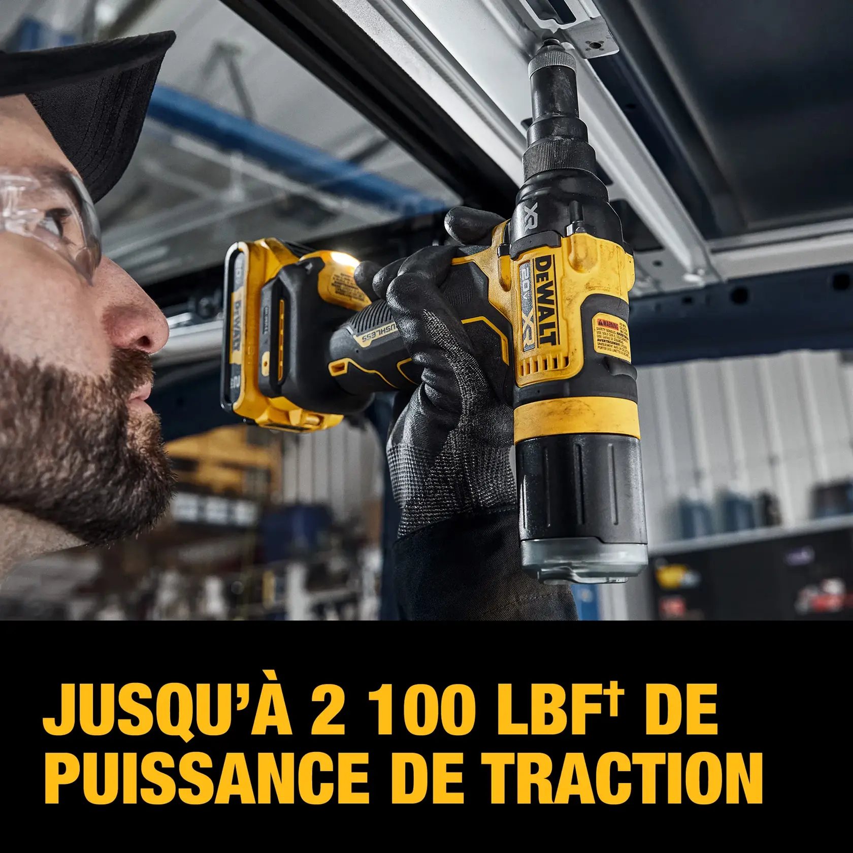 A gloved person uses a DEWALT cordless tool to install or remove a fastener from a metal surface indoors. The tool is highlighted, showing the DEWALT logo and product details. Text on the image reads: 'UP TO 2,100 LBF. OF PULLING FORCE.'