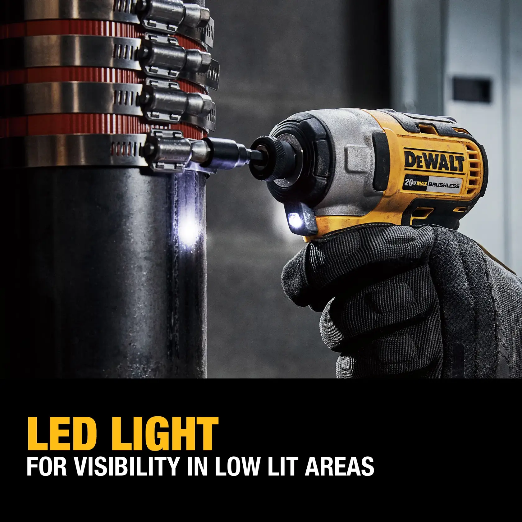 A DEWALT 20V MAX brushless cordless impact driver is being used by a gloved hand to work on a metal pipe in a dimly lit area. The tool's built-in LED light is illuminated to increase visibility.