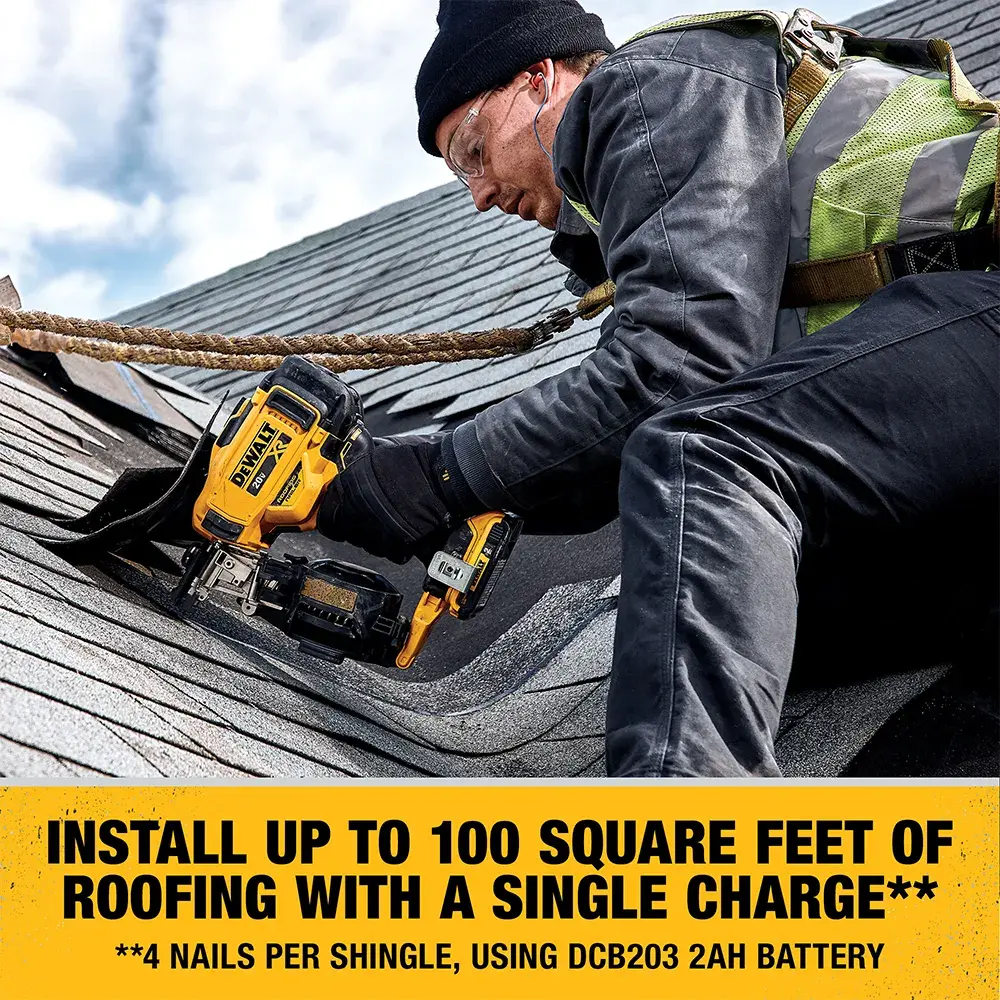A person wearing work gear uses a DEWALT cordless roofing nailer on a shingled roof. The text states that the tool can install up to 100 square feet of roofing with a single charge, based on 4 nails per shingle using a DCB203 2Ah battery.