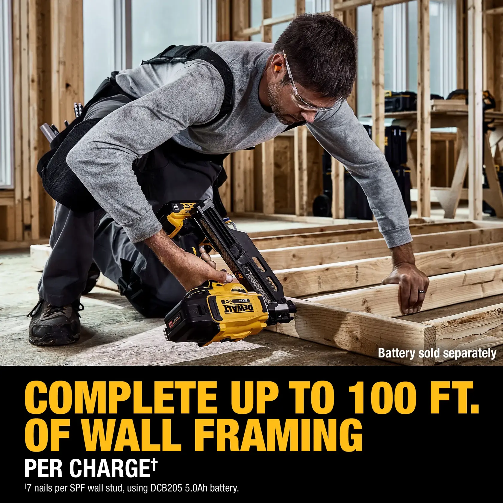 A person is kneeling on the floor of a building under construction, using a DEWALT cordless framing nailer (model DCN930B). The text highlights that the tool can complete up to 100 feet of wall framing per charge. The battery is sold separately.