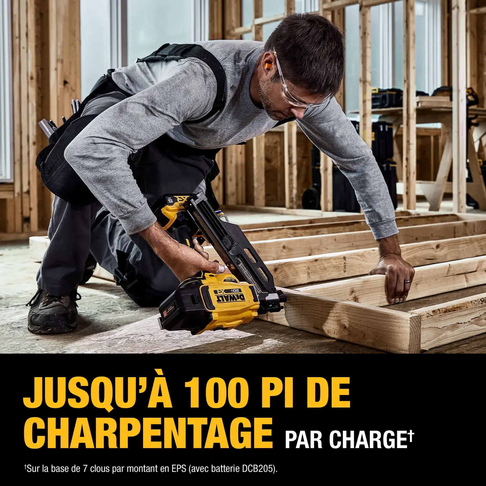 A person in protective glasses kneels in a construction area, using a DEWALT DCN930P1 cordless nailer to fasten wooden boards for wall framing. The image highlights the tool's capability to complete up to 100 feet of wall framing per battery charge. Construction materials and unfinished wooden framing are visible in the background.