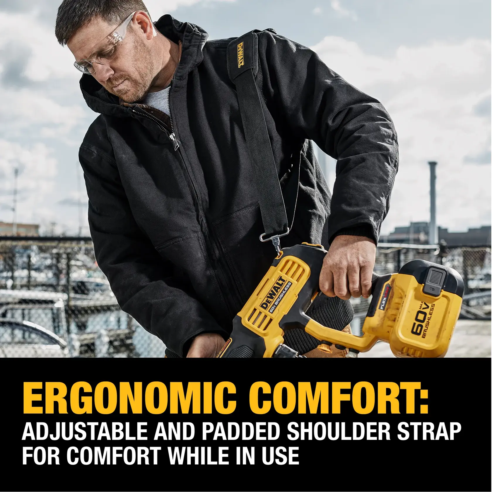 A person wearing a black jacket demonstrates a DEWALT power tool, holding it with an adjustable and padded shoulder strap for ergonomic comfort. The tool is yellow and black, and the background shows an outdoor industrial setting with fences and equipment. Text below highlights the ergonomic comfort and adjustability of the shoulder strap.