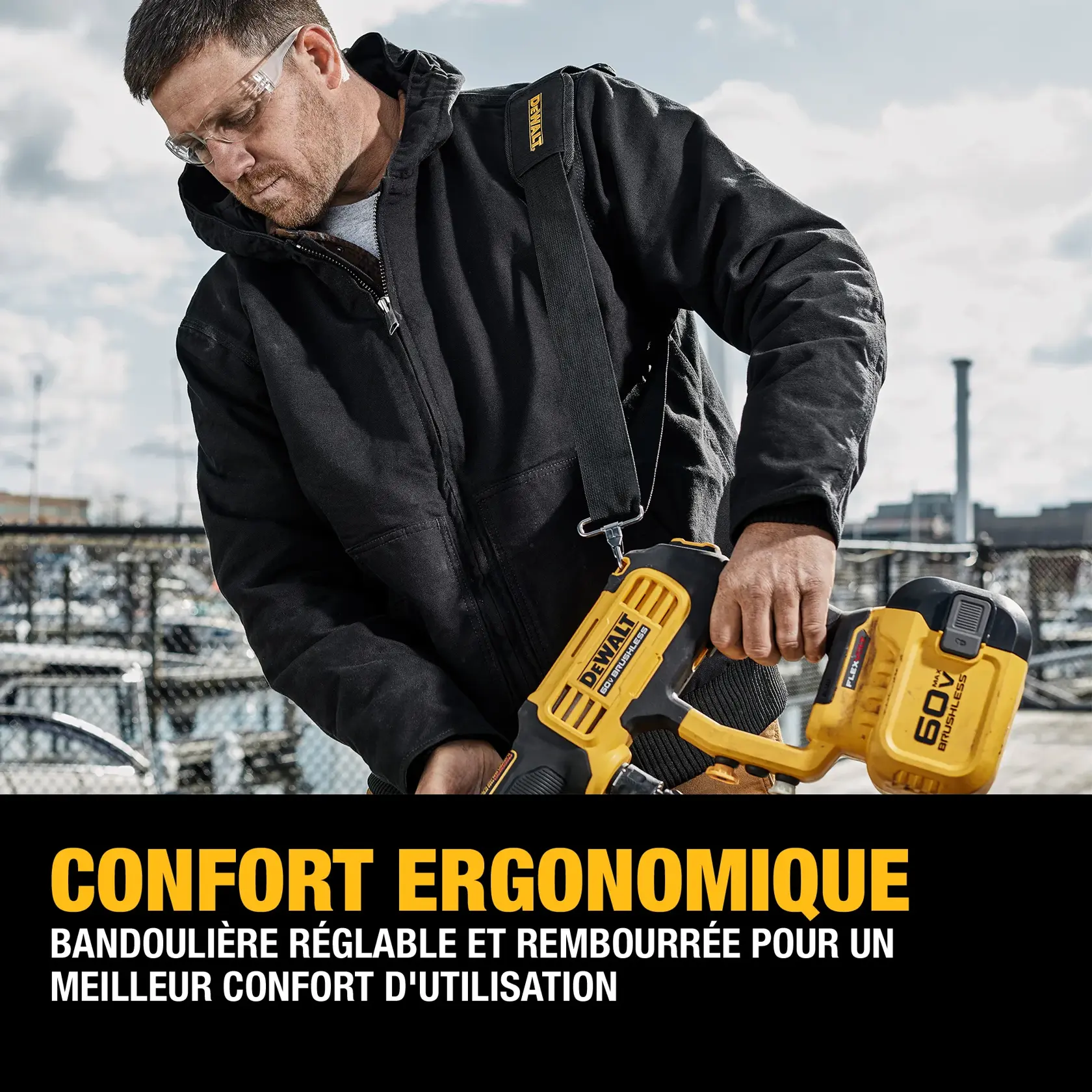 A person wearing a black jacket demonstrates a DEWALT power tool, holding it with an adjustable and padded shoulder strap for ergonomic comfort. The tool is yellow and black, and the background shows an outdoor industrial setting with fences and equipment. Text below highlights the ergonomic comfort and adjustability of the shoulder strap.