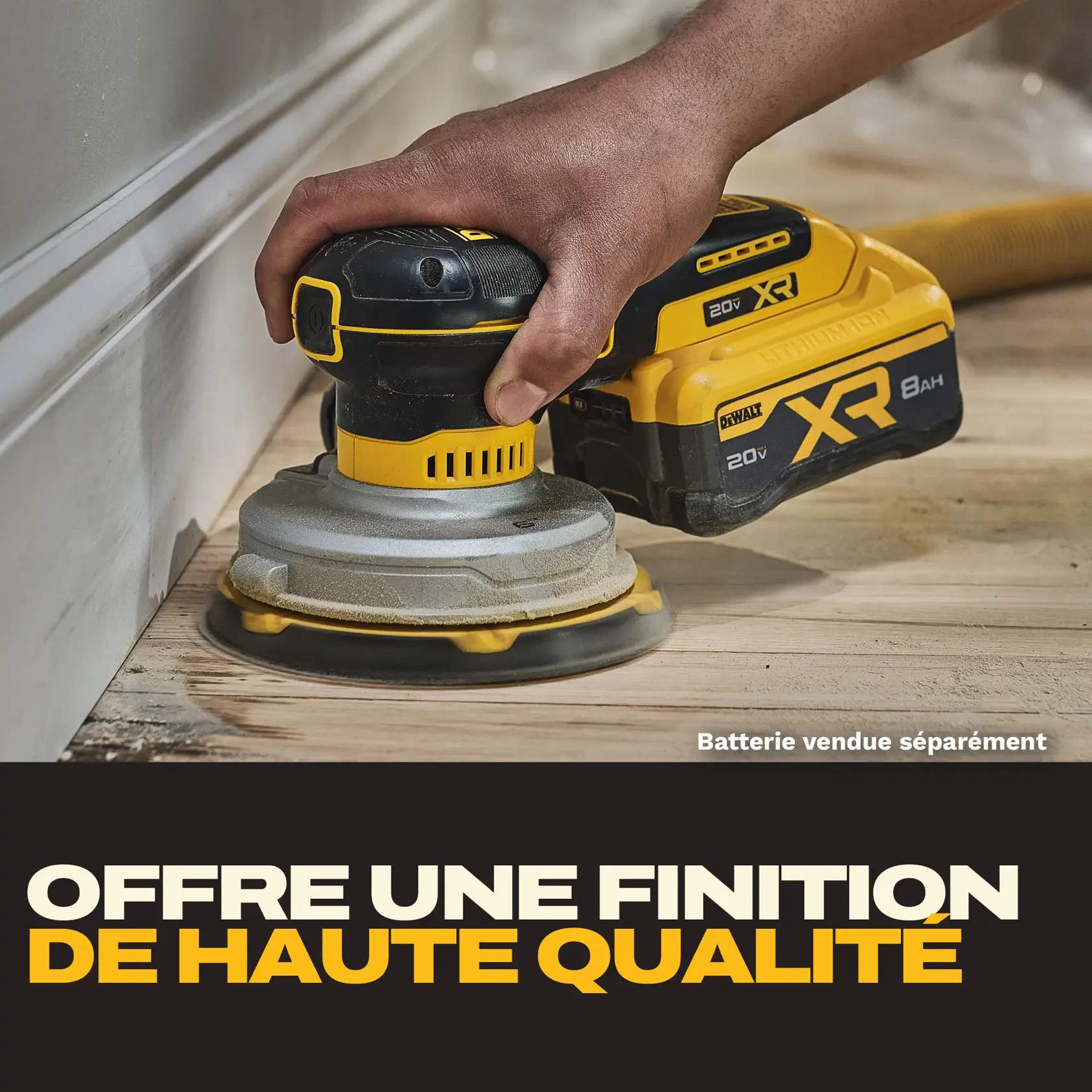 Gros plan d’une main utilisant une ponceuse sans fil DEWALT sur un sol en bois près d’une moulure murale blanche. La ponceuse porte le label XR et 20V, avec une note indiquant que la batterie est vendue séparément. Un texte en gras indique en dessous : « Offre une finition de haute qualité. »