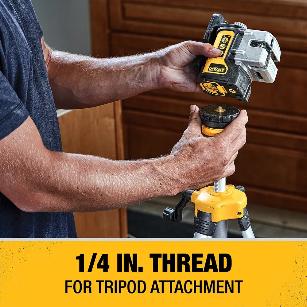 A person attaches a DEWALT laser level to a tripod using a 1/4 inch thread, with a yellow label below stating '1/4 IN. THREAD FOR TRIPOD ATTACHMENT'.