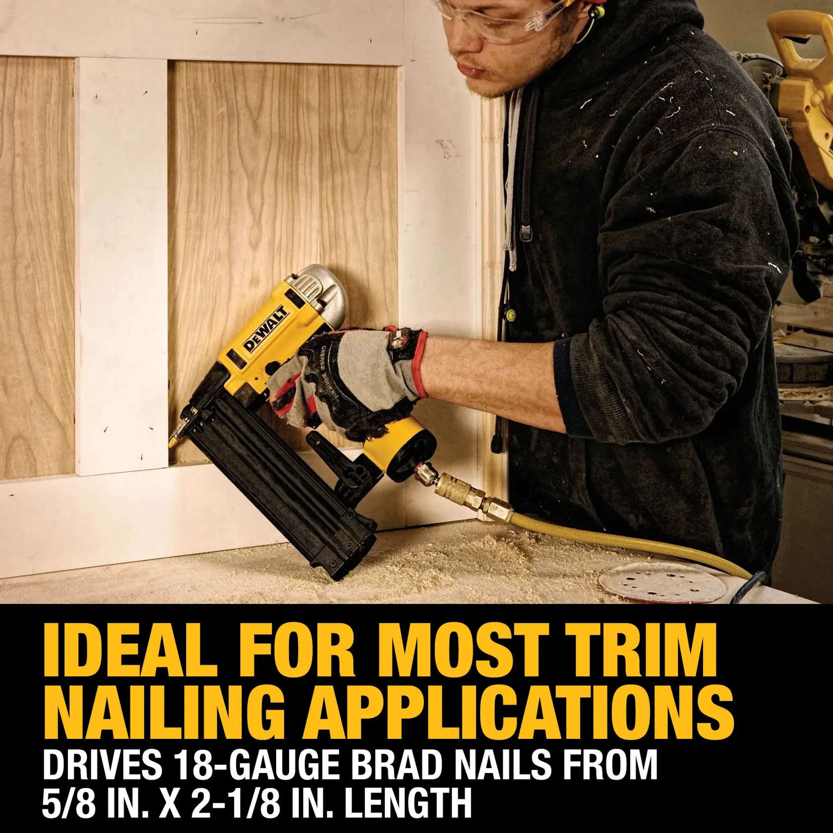 A person wearing safety glasses and gloves is using a DEWALT DWFP12233 pneumatic brad nailer to attach trim to a wooden surface. The image highlights that the tool is ideal for most trim nailing applications and can drive 18-gauge brad nails from 5/8 inch to 2-1/8 inch in length.