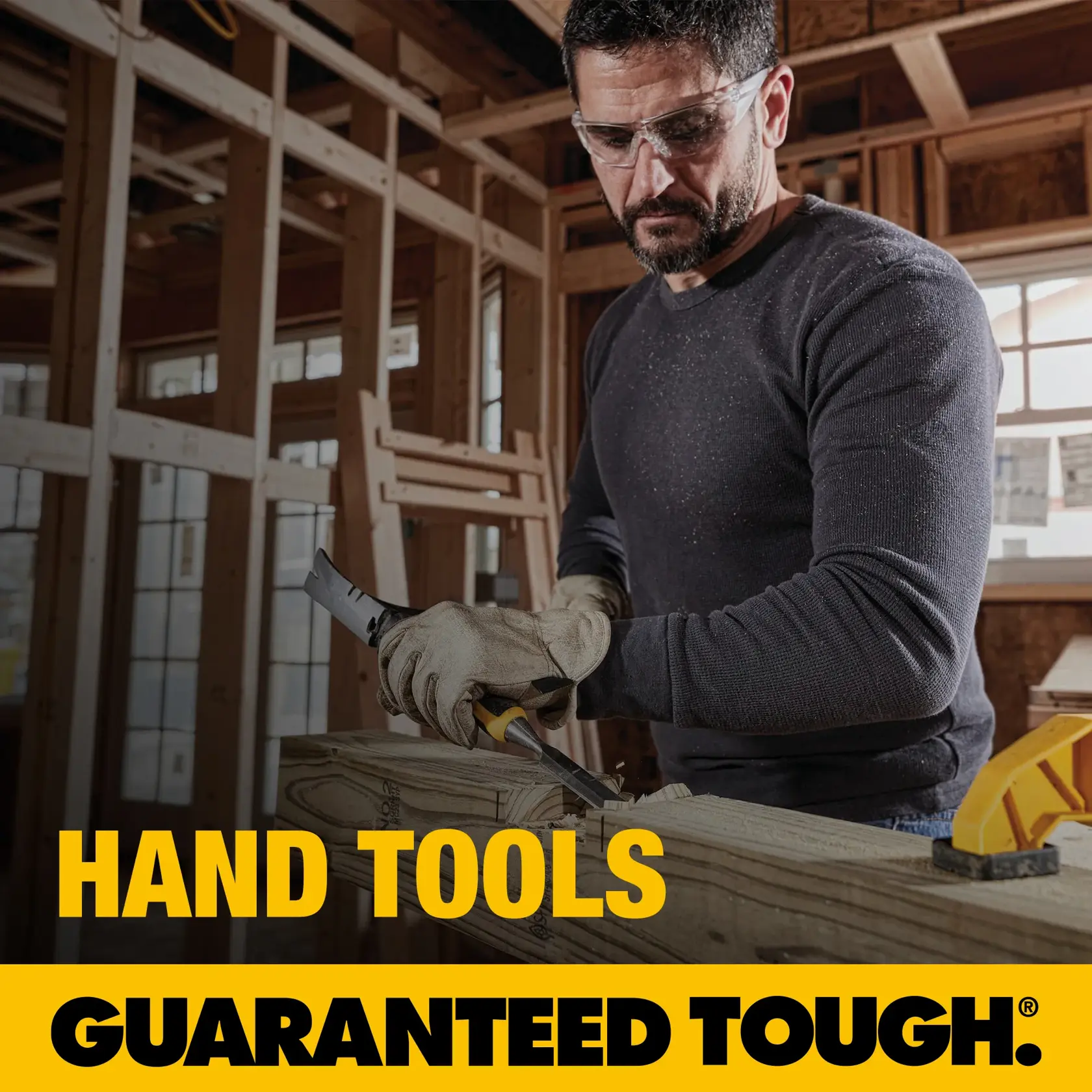 A person wearing gloves uses a hand tool to carve wood inside a framed structure. The image features bold yellow text that reads 'HAND TOOLS' and 'GUARANTEED TOUGH.'