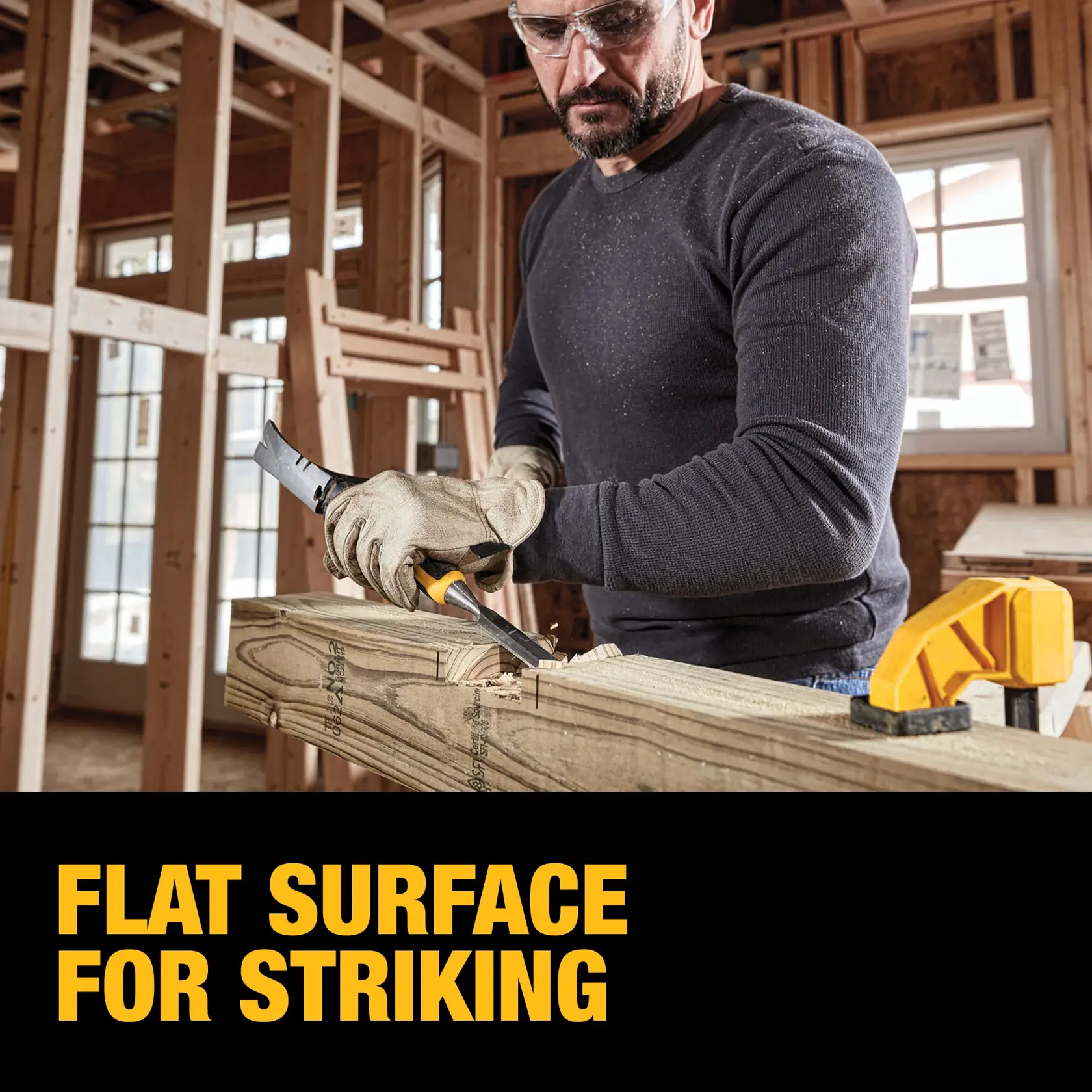 A person wearing gloves uses a DEWALT hand tool to work on a piece of wood in a construction setting. The image highlights the tool's flat striking surface. The text reads: 'FLAT SURFACE FOR STRIKING.'