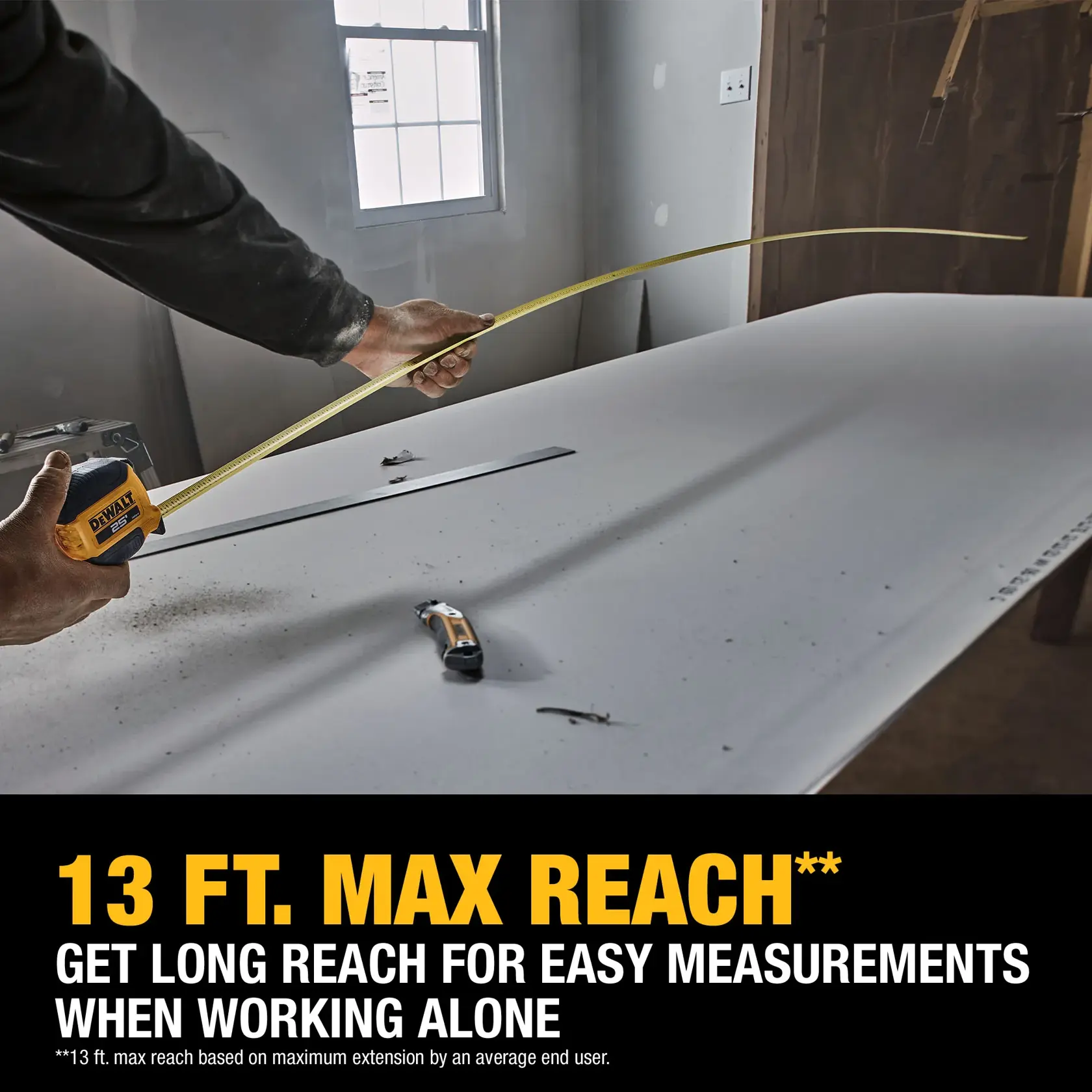 A person uses a DEWALT tape measure to measure a long board in a construction setting. The tape measure extends across the board and text highlights a 13 ft. maximum reach for easier measurements when working alone.