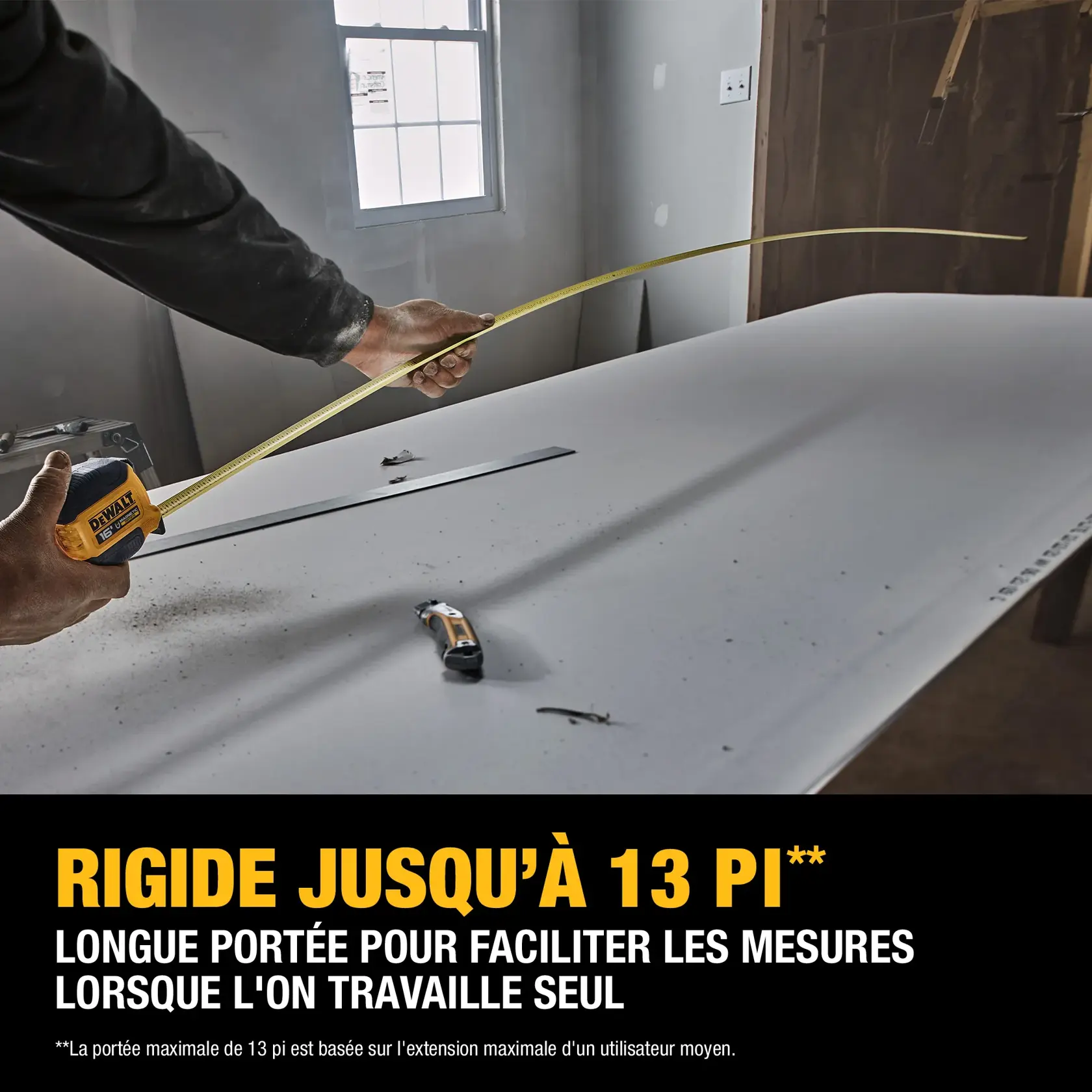 A person using a DEWALT tape measure to extend a measuring tape across a large work surface in a workshop or construction area, with text indicating '13 FT. MAX REACH' for easy measurements when working alone.