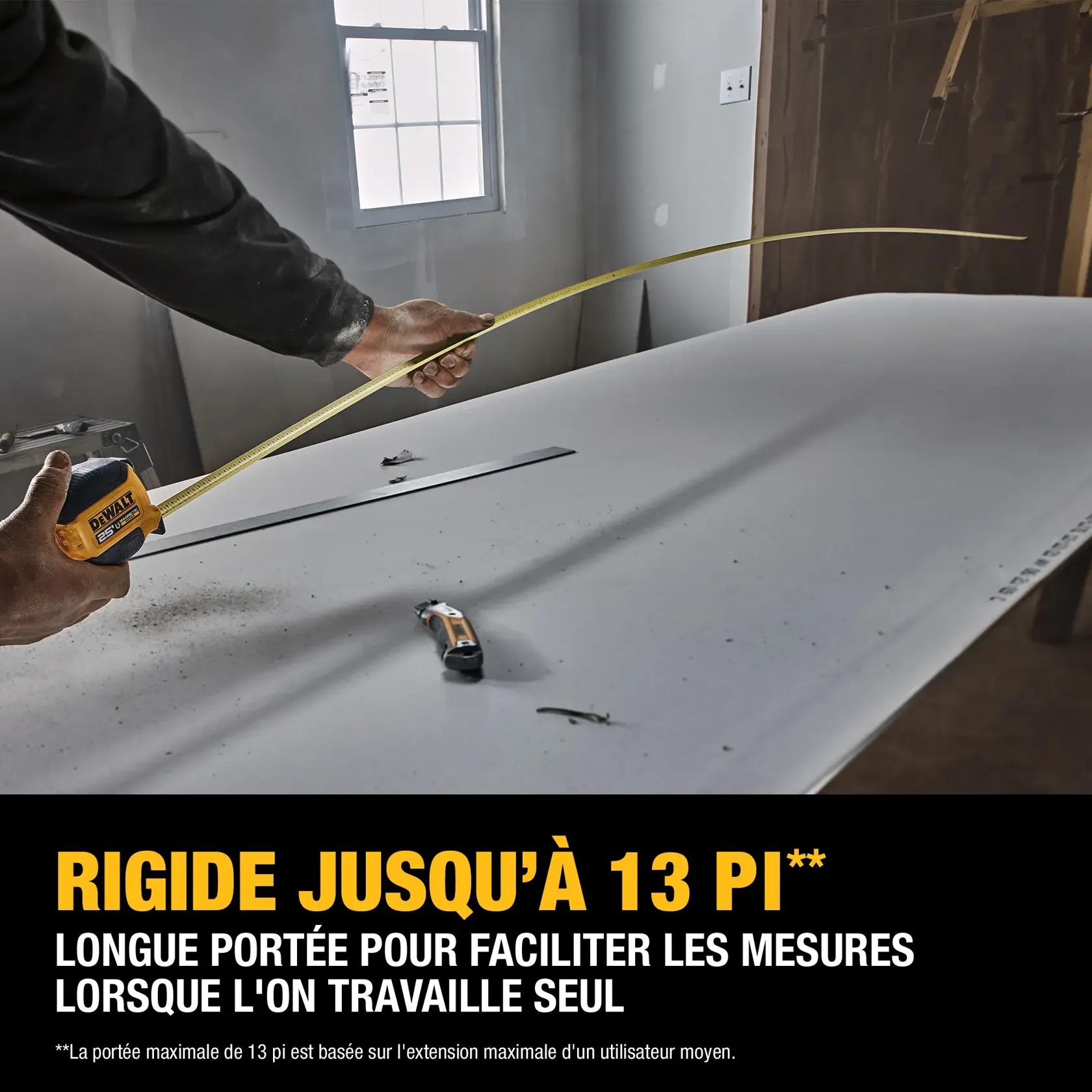 A person uses a DEWALT tape measure to measure a long distance across a large sheet of material. The tape measure is extended, demonstrating its maximum 13-foot reach. Construction tools and materials are visible in the workspace, with text highlighting the tape measure's long reach for easy measurements when working alone.