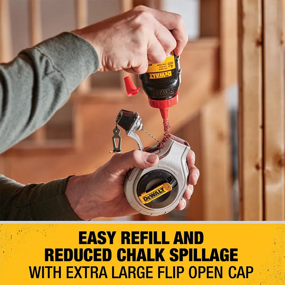 A person is refilling a DEWALT chalk line reel with red chalk powder using a DEWALT chalk refill bottle. The chalk line tool features an extra large flip open cap for easy refill and reduced chalk spillage. The background shows a wooden construction frame.
