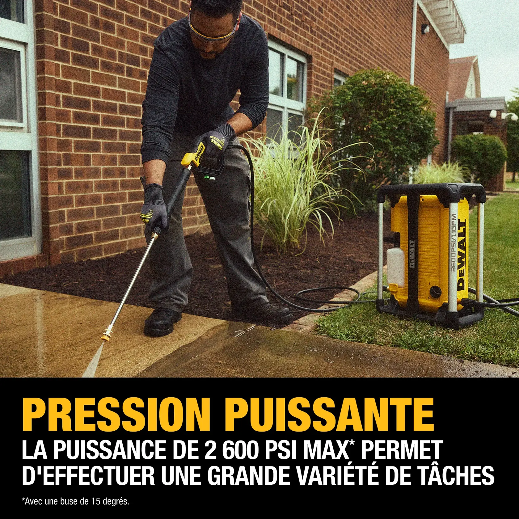A person using a DEWALT DWPW2600 pressure washer to clean a concrete walkway outside a brick building. The washer is shown spraying water with strong pressure. The text highlights 'Powerful Pressure' with 2,600 max PSI output, and there is a yellow DEWALT pressure washer unit visible on the grass.