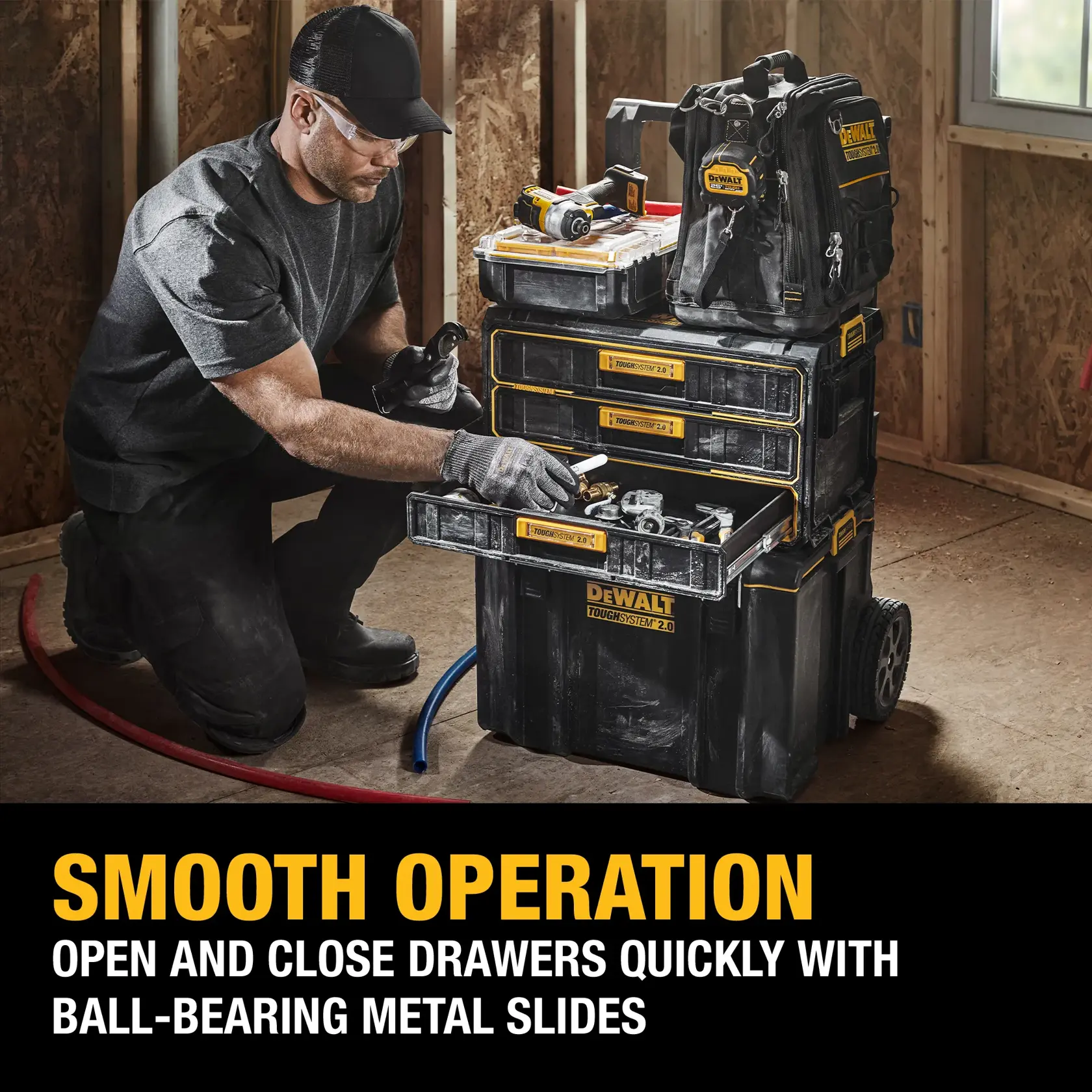 A person in work attire is kneeling next to a DEWALT ToughSystem 2.0 mobile tool storage unit with multiple drawers and containers. The tool storage is open, showing various tools and accessories inside. The unit is described as having smooth operation with ball-bearing metal slides for easy opening and closing of drawers.