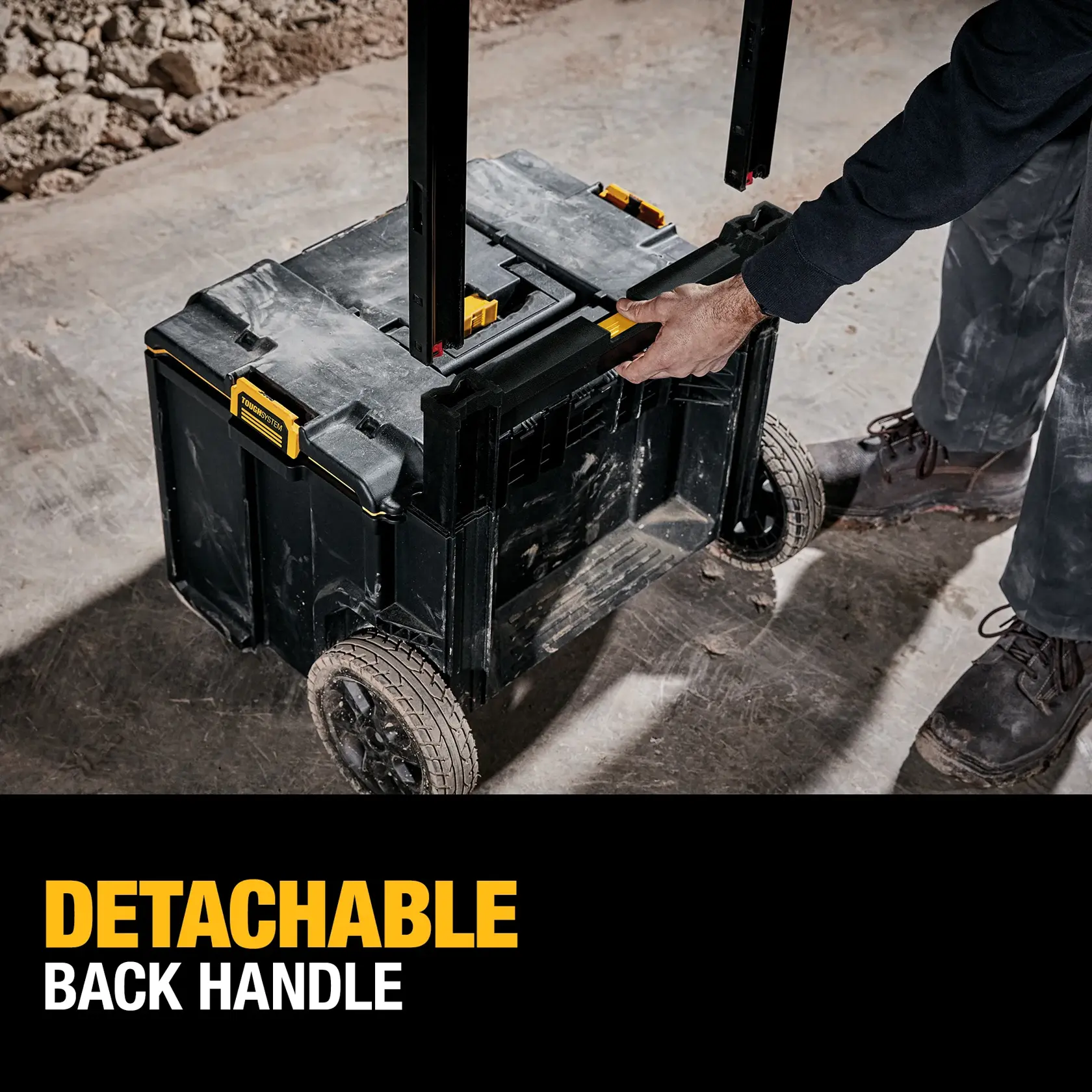 A person is holding the detachable back handle of a DEWALT rolling tool box with large wheels, on a construction site. The text says 'DETACHABLE BACK HANDLE'.