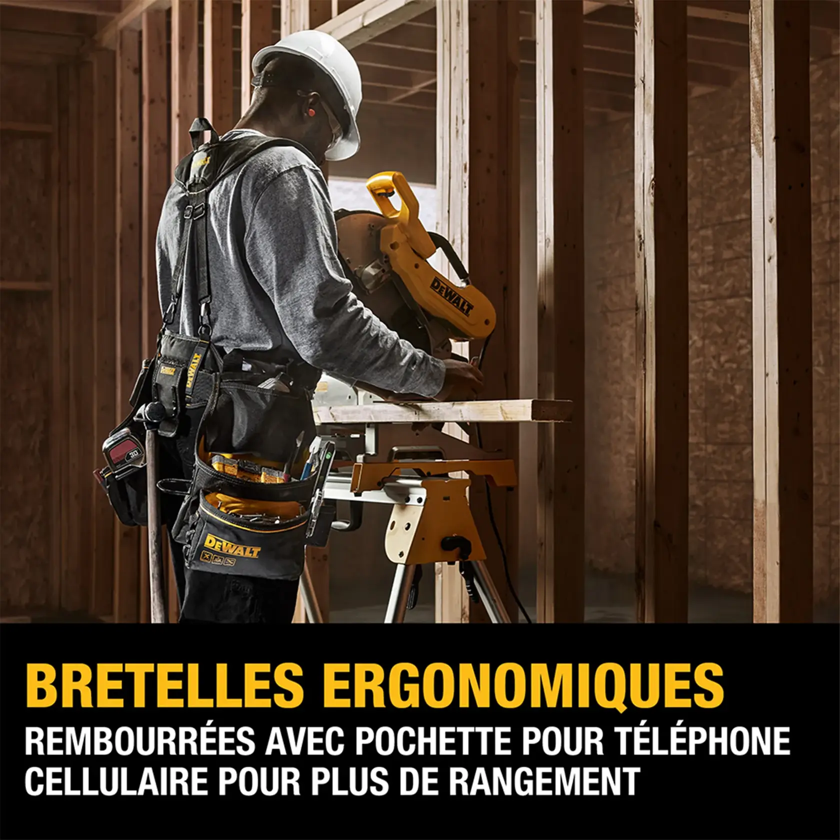 A construction worker wearing ergonomic padded suspenders and a tool belt, working with a DEWALT miter saw at a wood-framed building site. The suspenders include a cell phone pocket for extra storage. Text overlay reads: 'Ergonomic Suspenders. Padded suspenders feature a cell phone pocket for extra storage.'