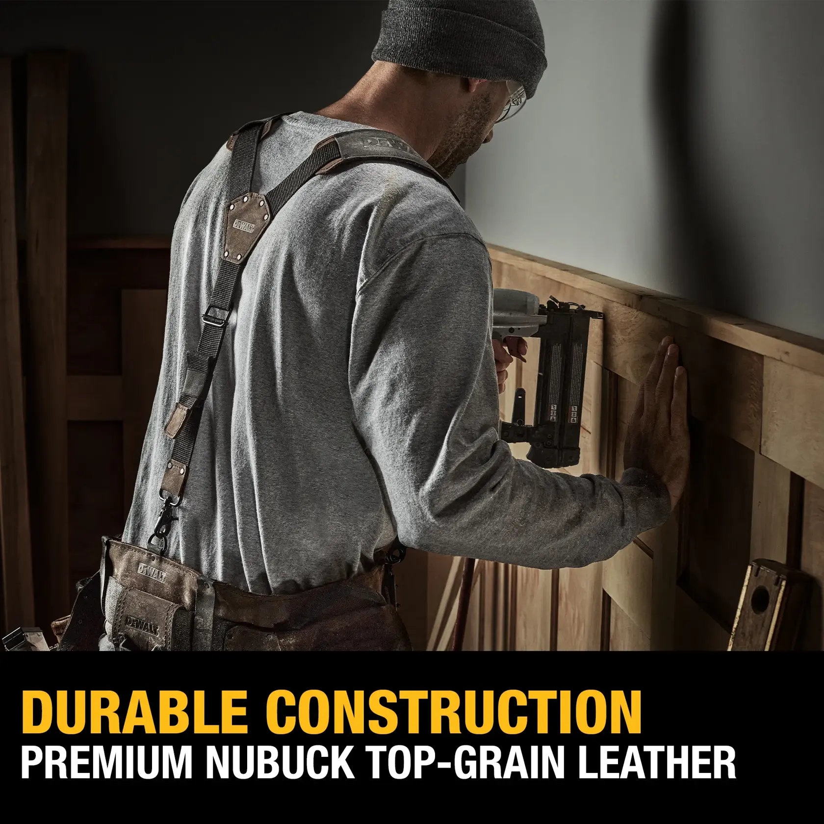 A person wearing a DEWALT work apron is using a power tool to work on a wooden wall. The apron is made of premium nubuck top-grain leather. Text reads: 'Durable Construction. Premium Nubuck Top-Grain Leather.'