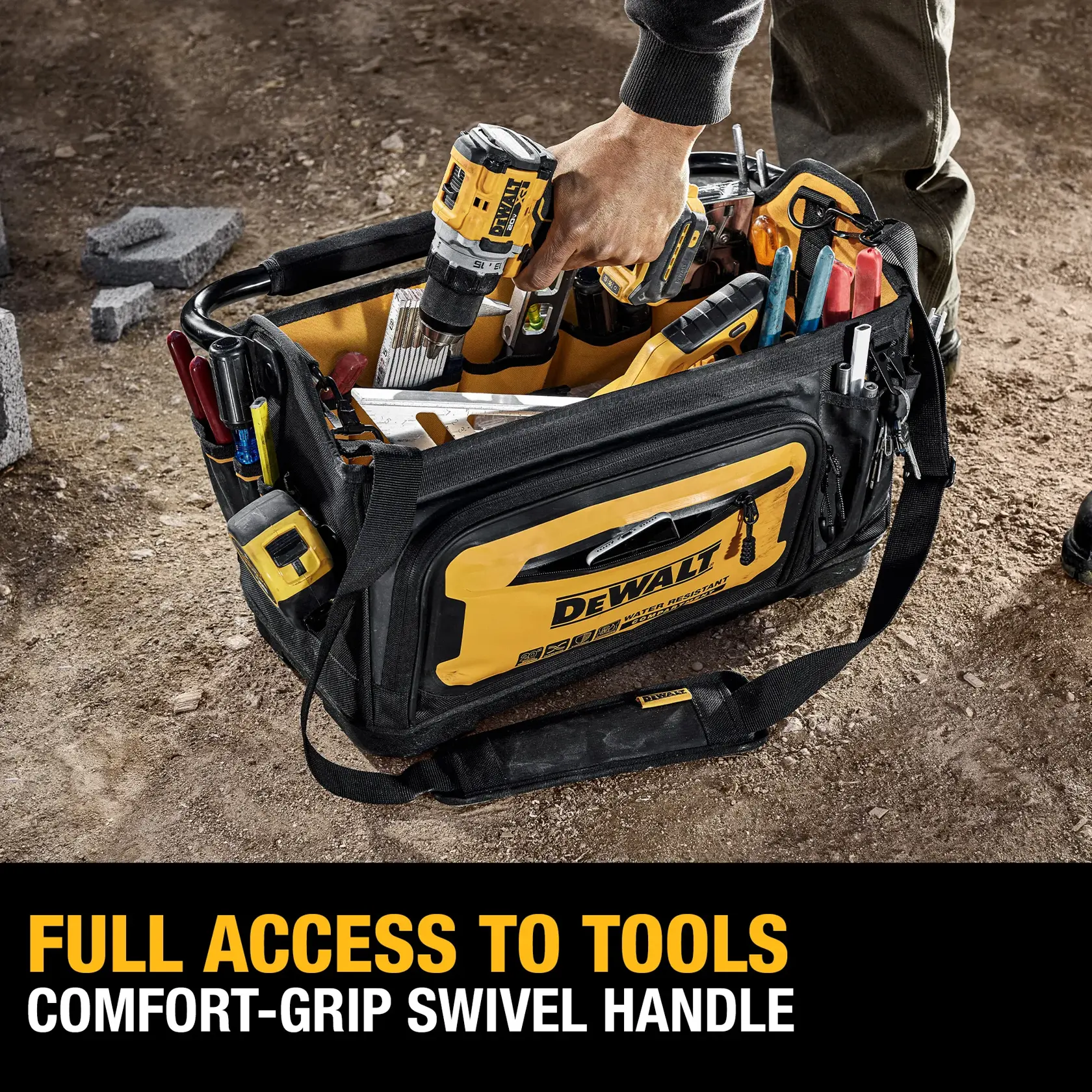 A DEWALT-branded tool bag on a worksite, filled with various hand tools and a power drill. A person's hand is reaching into the bag. The bag is designed for full access to tools and features a comfort-grip swivel handle. Text on the image reads: 'FULL ACCESS TO TOOLS, COMFORT-GRIP SWIVEL HANDLE.'