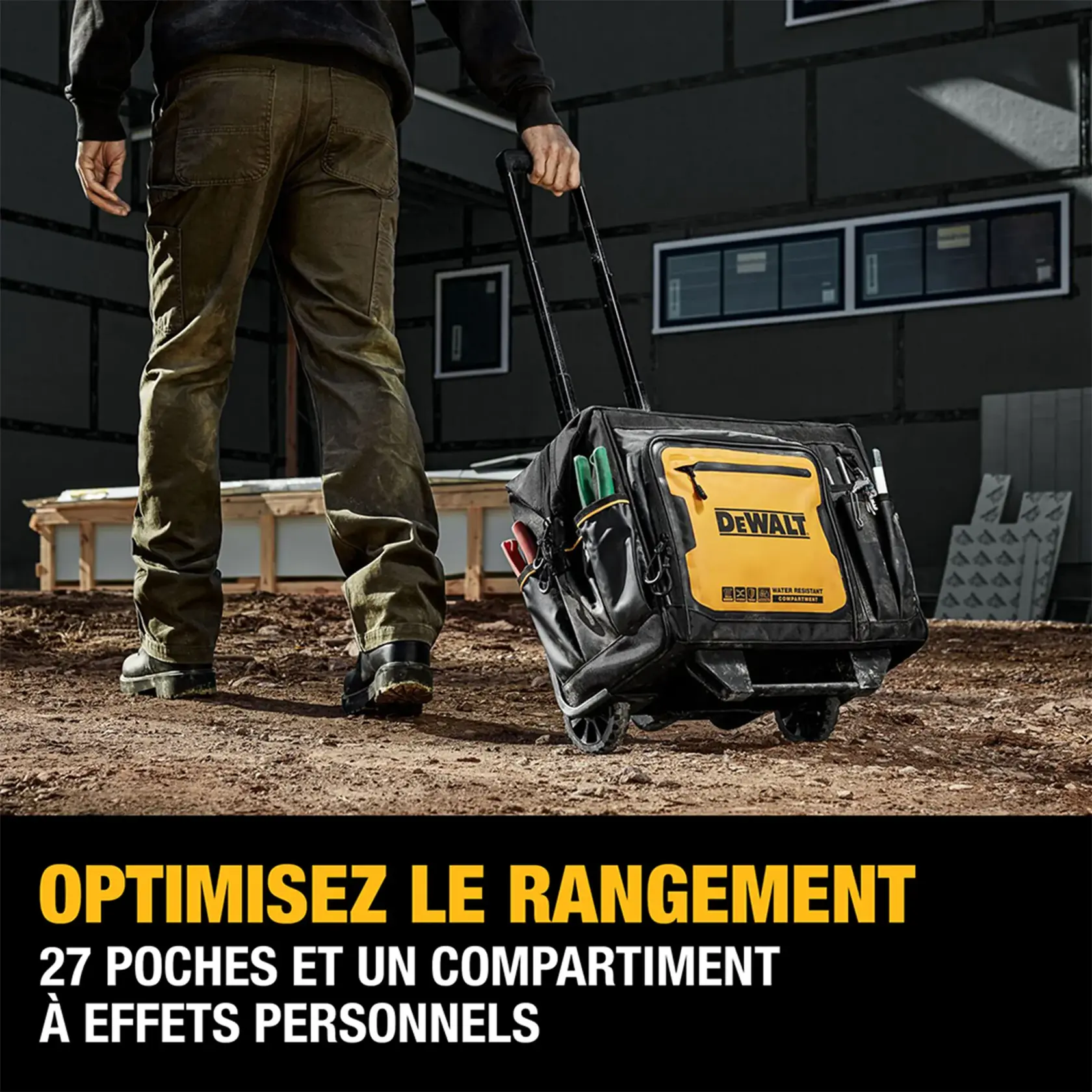 A person pulls a DEWALT rolling tool bag with an extendable handle outdoors at a construction site. The bag is black and yellow, featuring multiple exterior pockets filled with tools. Promotional text below highlights storage optimization, 27 pockets, and a personal effects compartment.