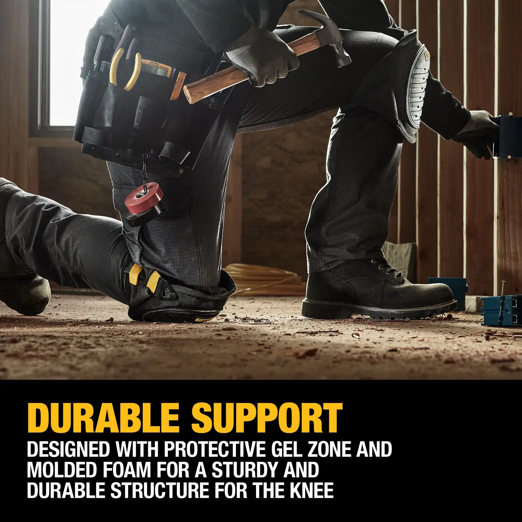 A person wearing black work pants, black boots, gloves, and a tool belt is kneeling on a construction site floor. The individual is wearing protective knee pads and holding a hammer, working near exposed wooden framing. Text on the image promotes durable support from protective gel zones and molded foam for sturdy knee protection.
