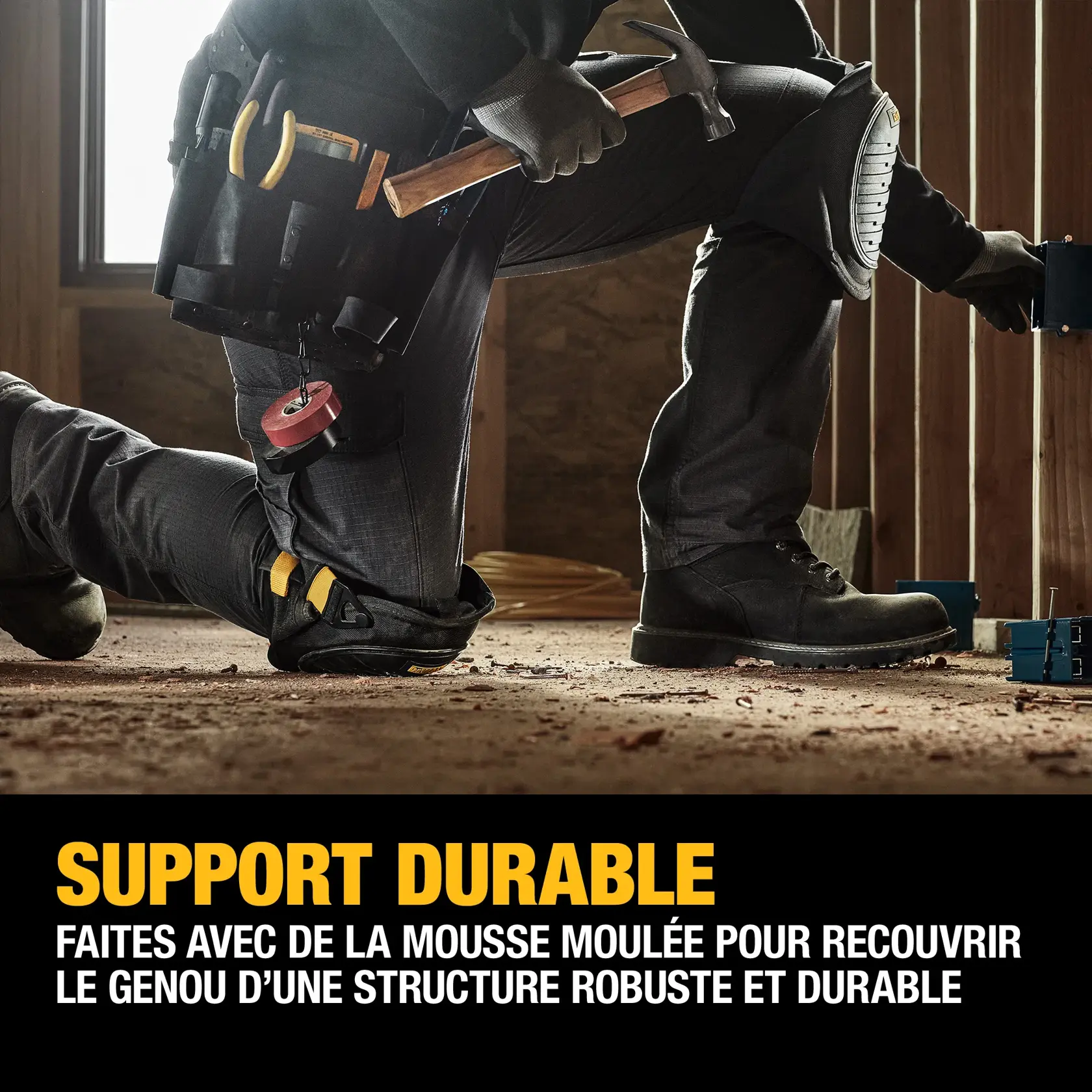 A person wearing black work pants, black boots, gloves, and a tool belt is kneeling on a construction site floor. The individual is wearing protective knee pads and holding a hammer, working near exposed wooden framing. Text on the image promotes durable support from protective gel zones and molded foam for sturdy knee protection.