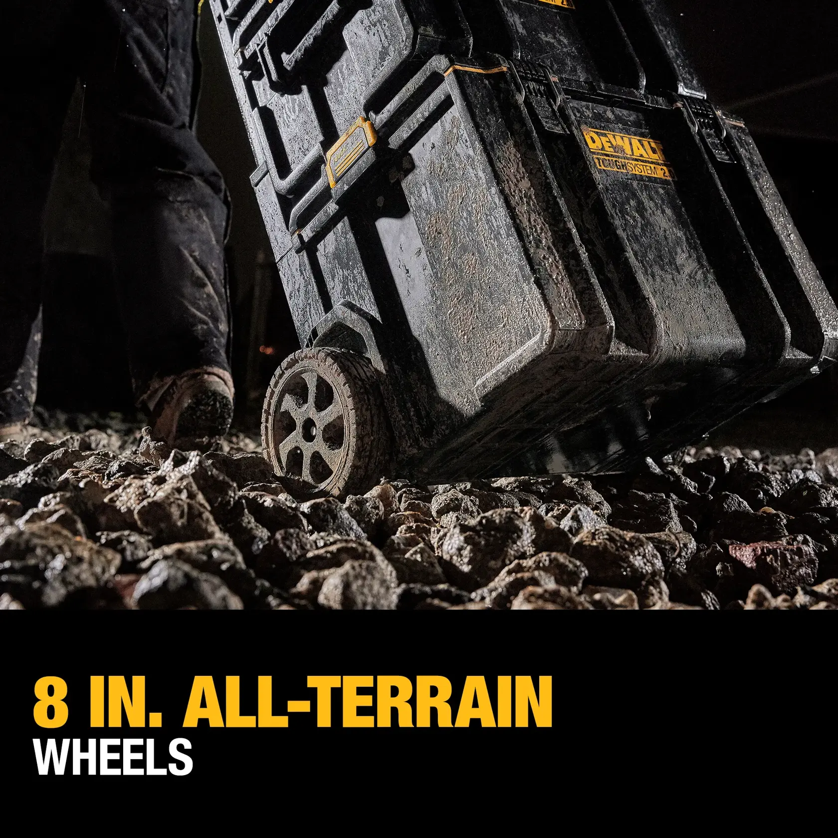 Close-up of a DEWALT ToughSystem rolling tool storage box being wheeled over rough, rocky terrain, emphasizing its durable 8-inch all-terrain wheels.