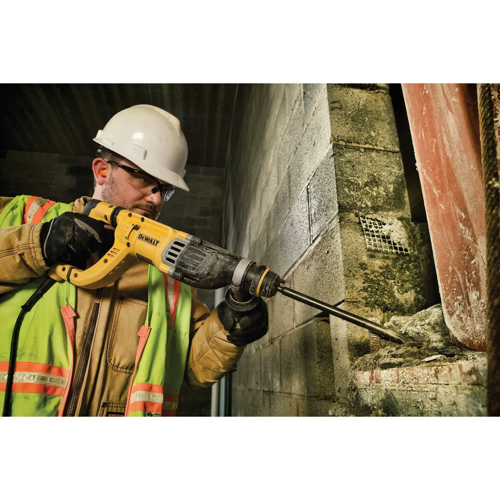A construction worker wearing a safety helmet and reflective vest uses a DEWALT rotary hammer drill (model D25263K) to chisel concrete in an industrial setting.