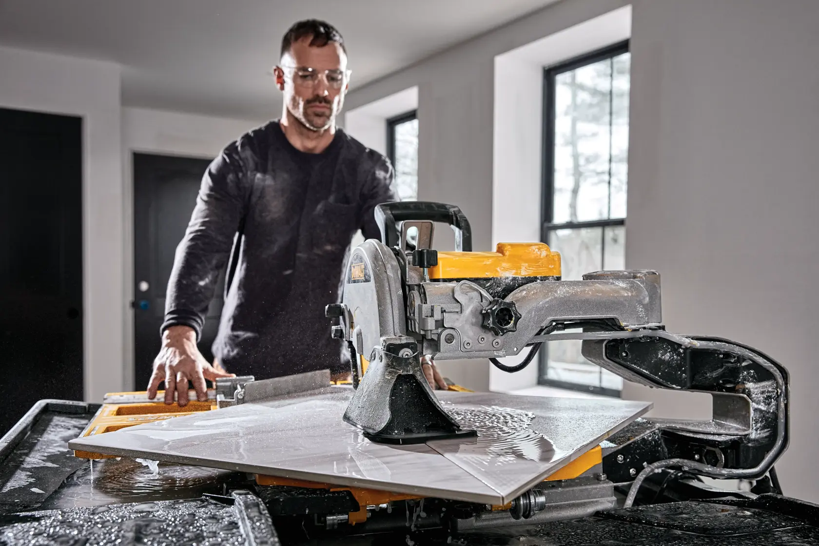 A person using a DEWALT tile saw model D36000S to cut a large tile indoors. The saw is wet and the person’s face is blurred for privacy.