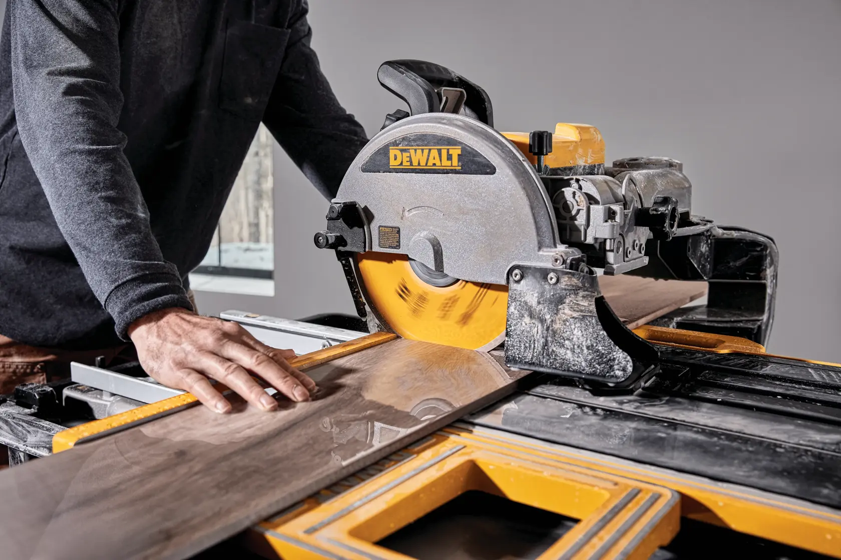 A person using a DEWALT tile saw to cut a piece of wood or tile in a workshop setting.