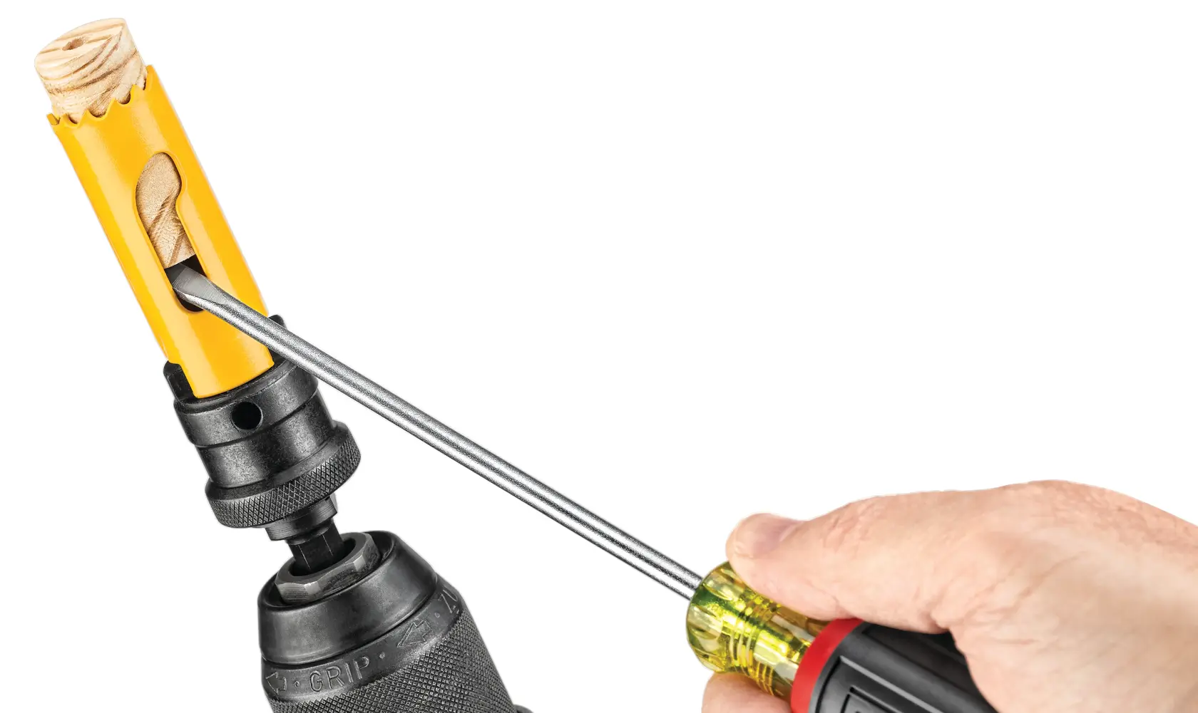 A close-up view of a person using a screwdriver to remove wood debris from a yellow hole saw attached to a drill.