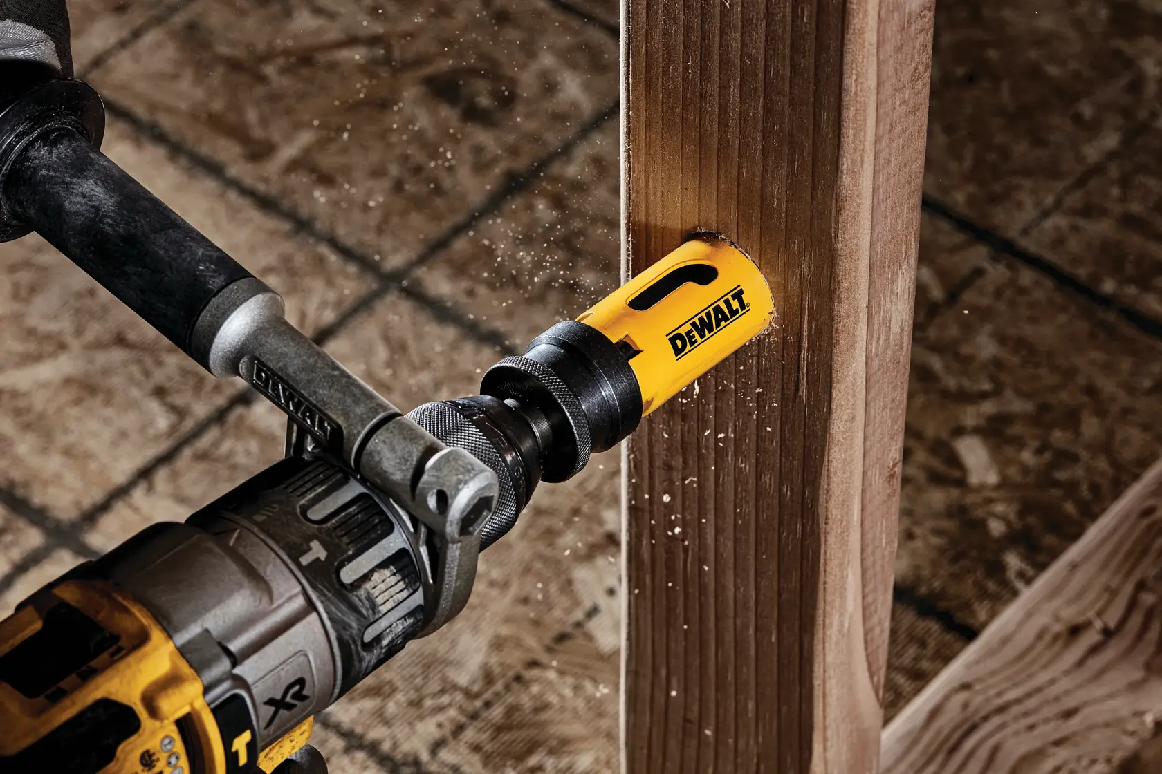 A DEWALT hole saw attached to a power drill is cutting a circular hole in a wooden beam, with wood shavings visible.