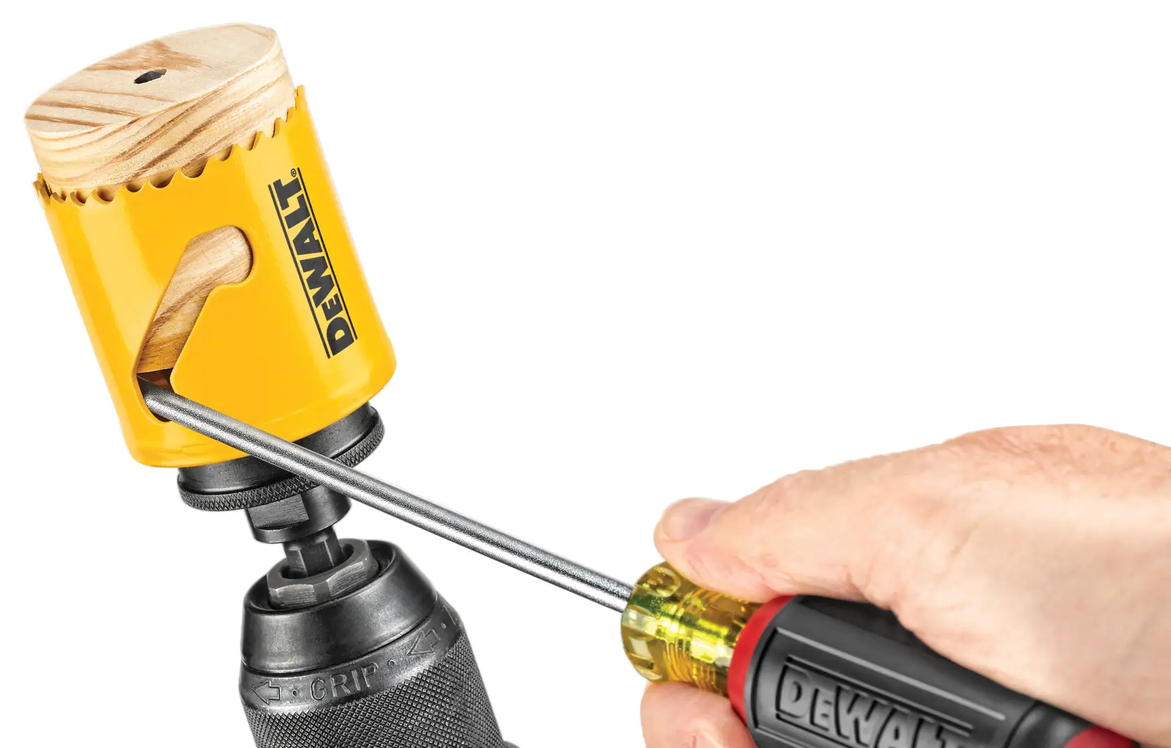 A close-up of a hand using a screwdriver to remove a wooden cylinder from a yellow DEWALT hole saw attached to a drill.