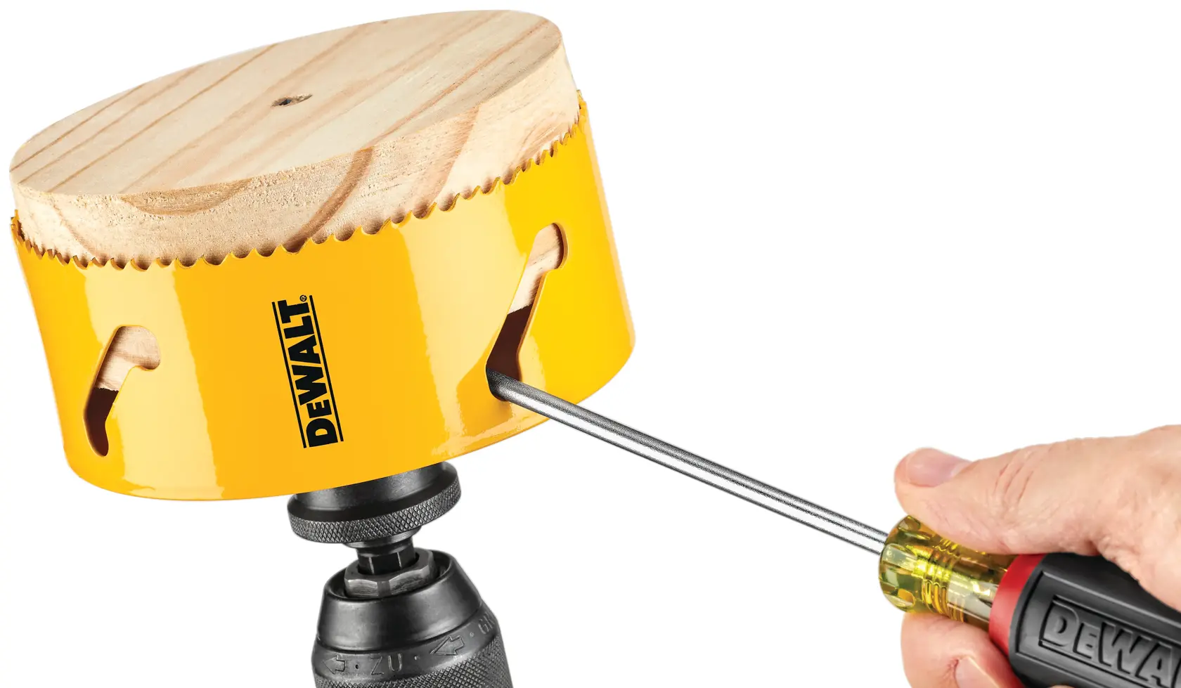 A person uses a DEWALT screwdriver to remove a wooden disk from a yellow DEWALT hole saw attached to a drill.