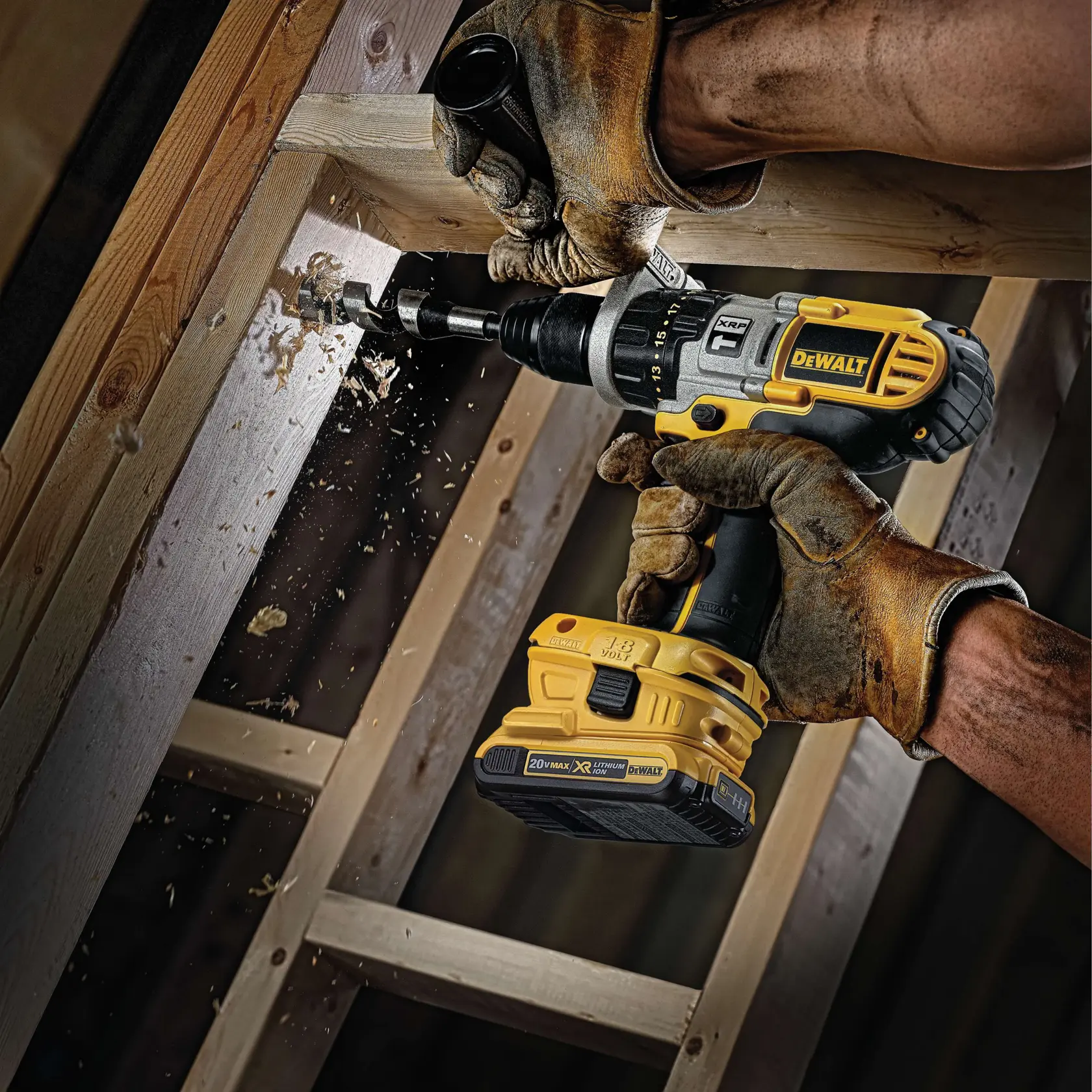 A person wearing brown work gloves uses a DEWALT cordless power drill to bore a hole in a wooden beam, with wood shavings flying from the drilling process.
