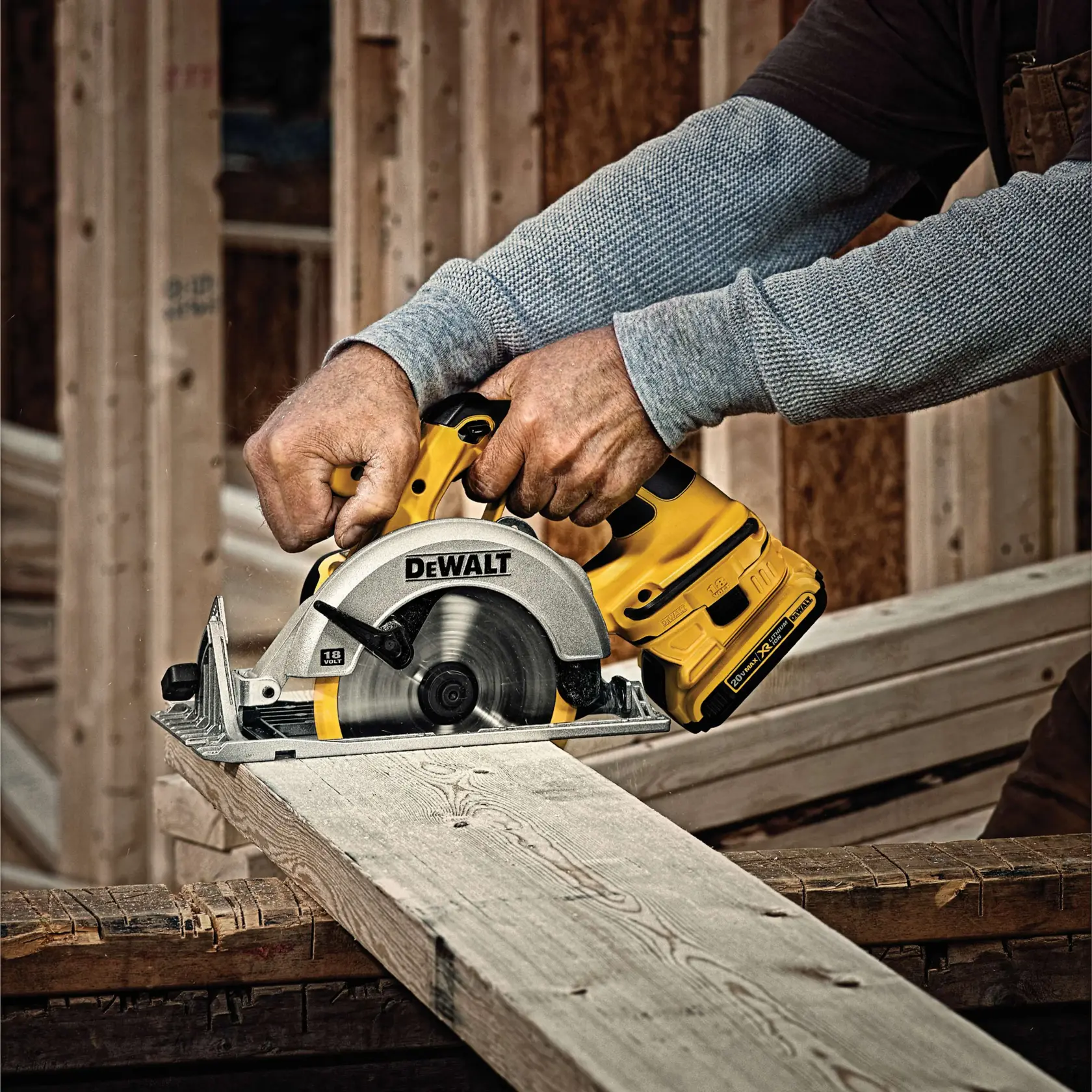 A person using a yellow DEWALT cordless circular saw to cut a wooden plank at a construction site.