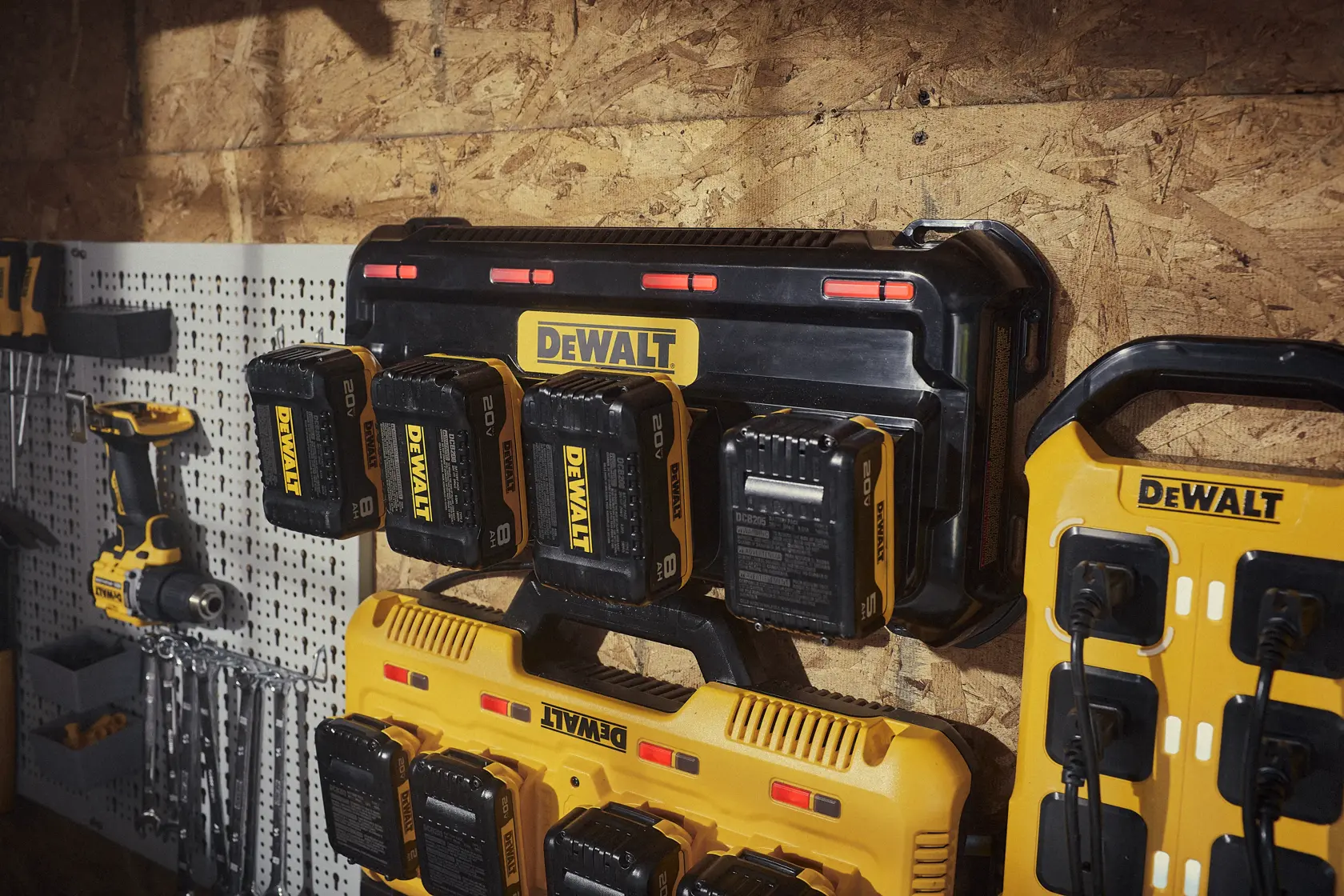 A DEWALT battery charging station mounted on a wooden wall, with several DEWALT 20V batteries inserted. Various DEWALT tools and accessories are visible nearby, including a drill and other chargers.