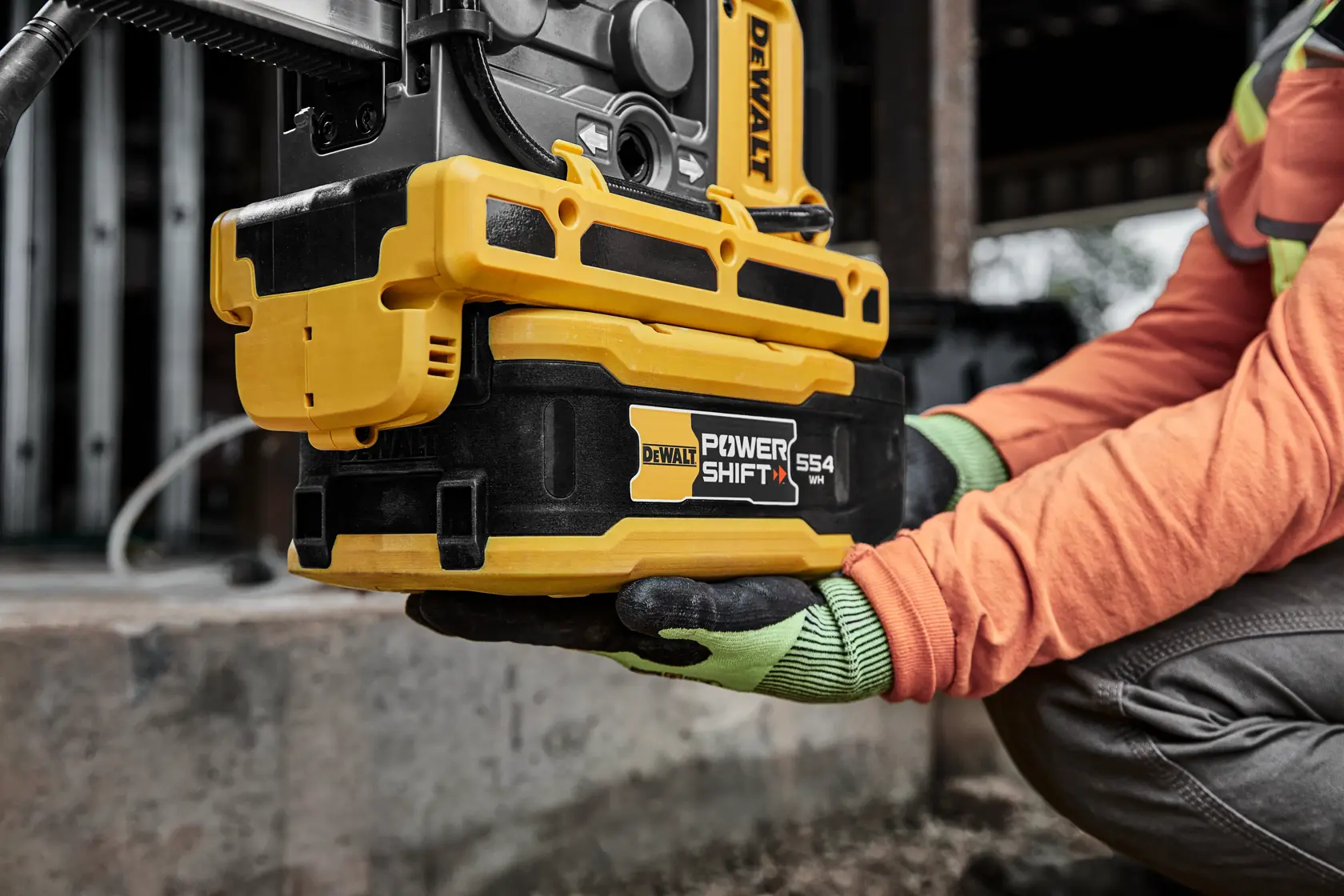 Close-up of a worker holding a DEWALT Power Shift 554 tool with gloves, showing the product in use at a construction site.