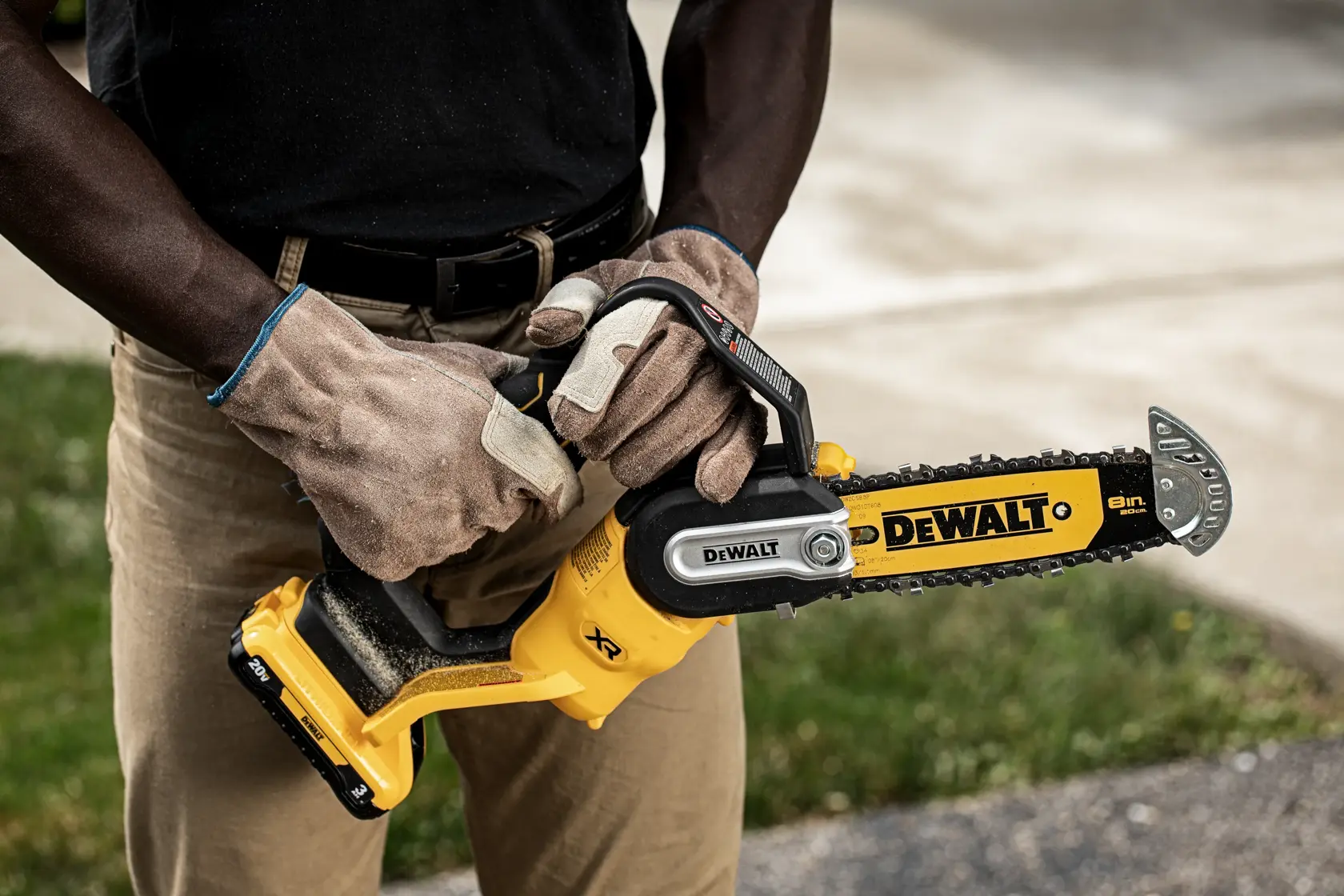 A person wearing work gloves holds a DEWALT 8-inch cordless chainsaw outdoors. The yellow and black tool features the DEWALT logo and a visible battery pack.