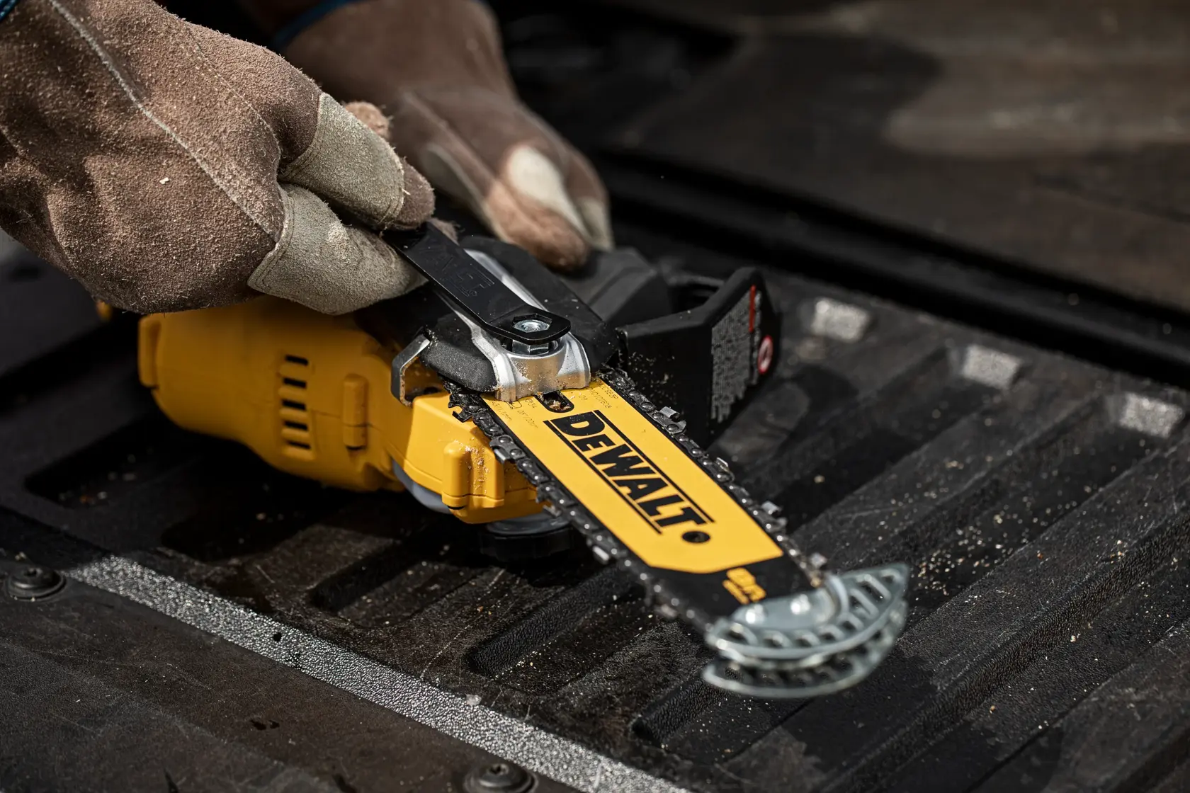 Close-up of a person wearing gloves adjusting the chain tension on a yellow DEWALT cordless chainsaw placed on a black surface.