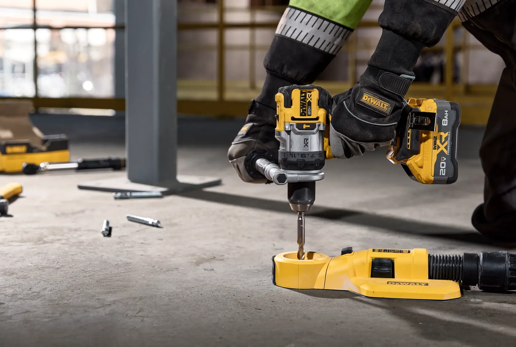 Gloved hand using a DEWALT cordless drill on a concrete floor at a work site, with tools and bolts scattered nearby.