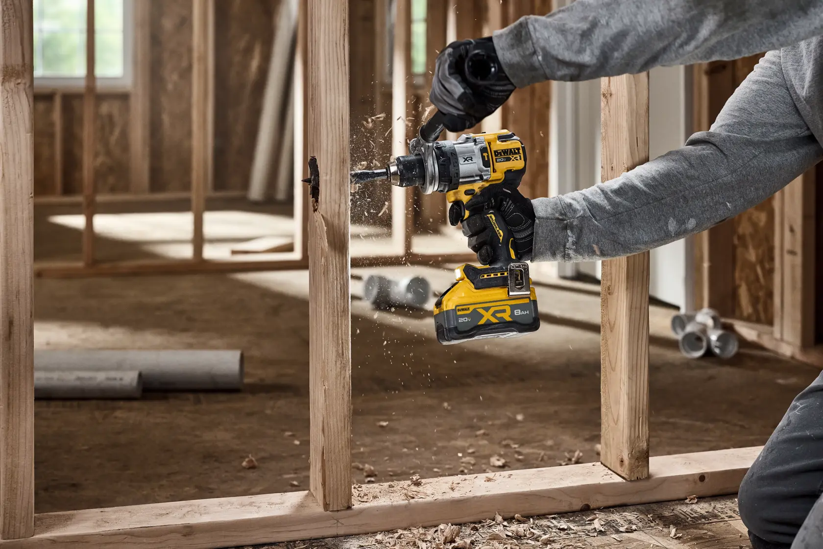 A person using a DEWALT cordless power drill to bore a hole into a wooden frame at a construction site. Wood shavings are visible as the drill operates.