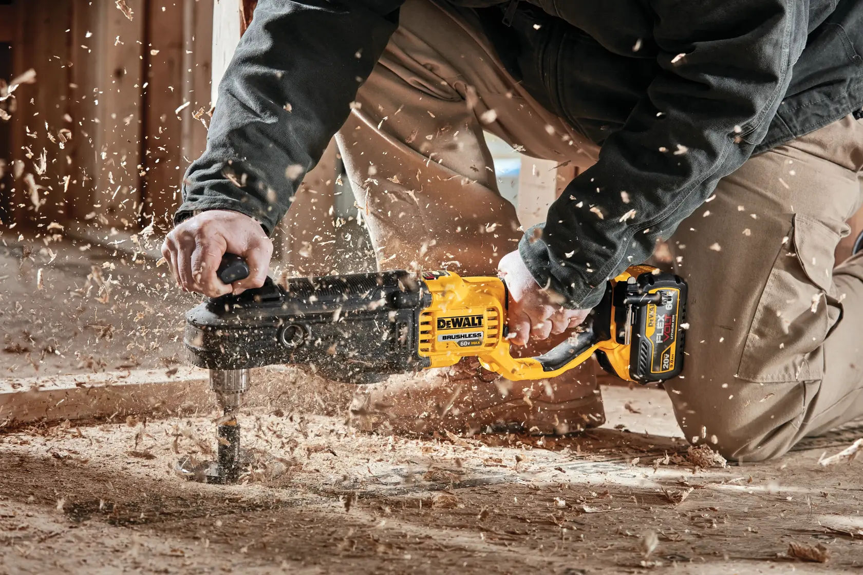A person using a DEWALT cordless brushless drill to bore a hole in a wooden surface, with wood chips and debris flying around.