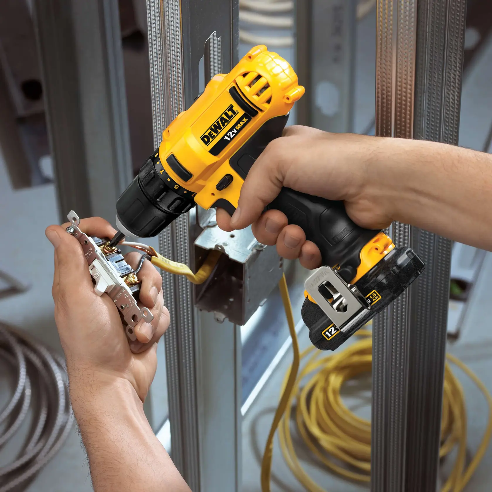 A person uses a DEWALT 12V cordless drill to install wiring components in a metal electrical box framework at a construction site.