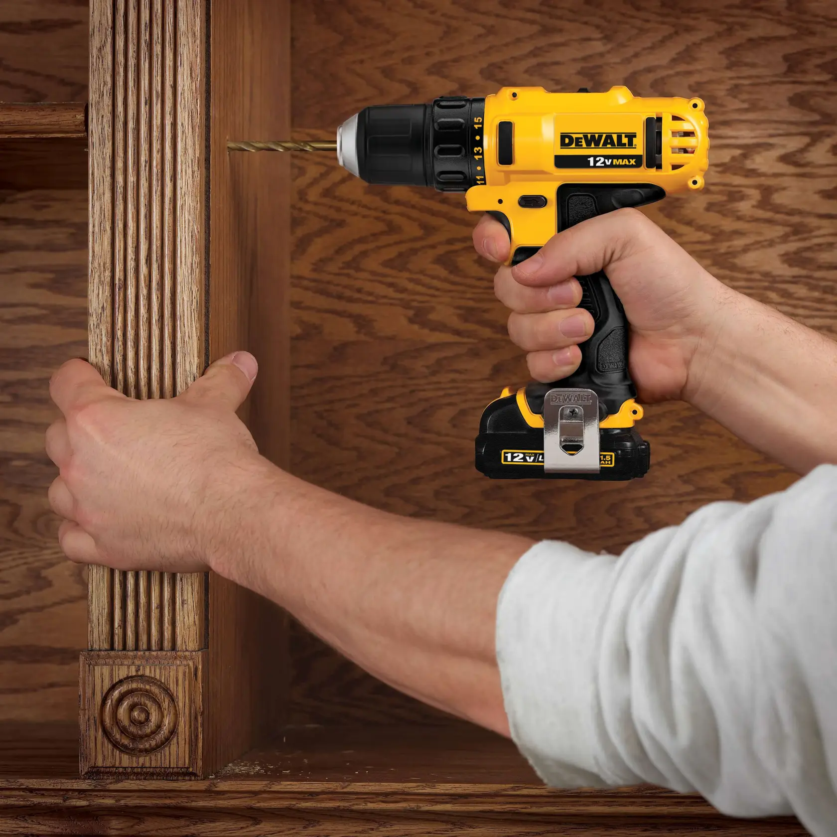 A person uses a yellow and black DEWALT 12V MAX cordless drill to drill into a wooden cabinet.