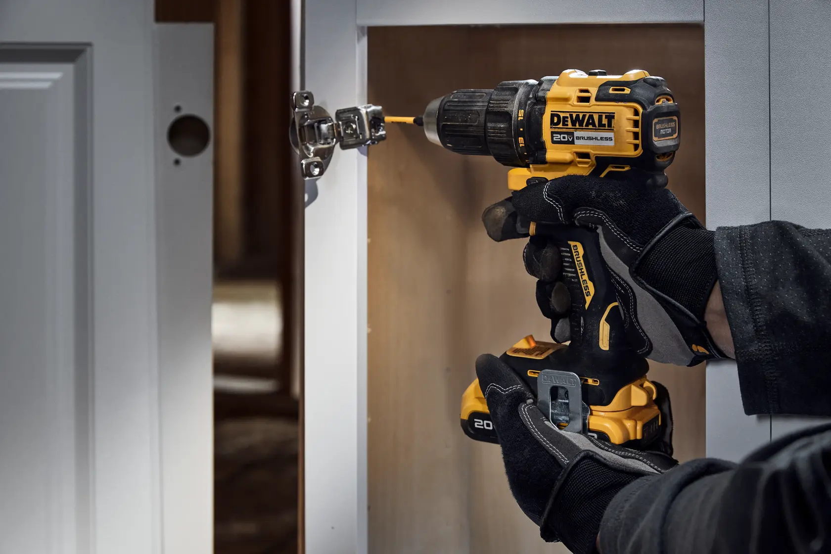 A person wearing black gloves uses a DEWALT cordless drill to install or adjust hardware on a cabinet door.