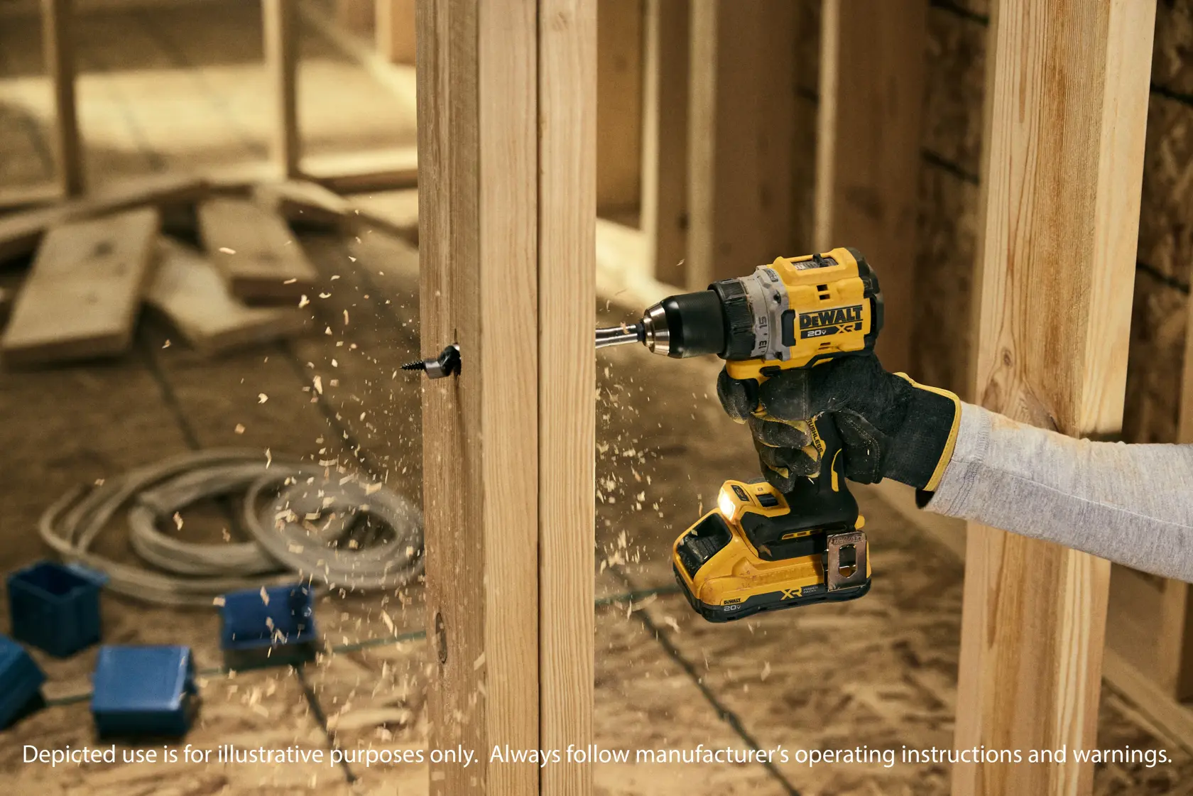A person wearing work gloves uses a DEWALT cordless drill to drill a hole into a wooden beam at a construction site. Wood shavings are visible as the drill is in operation.