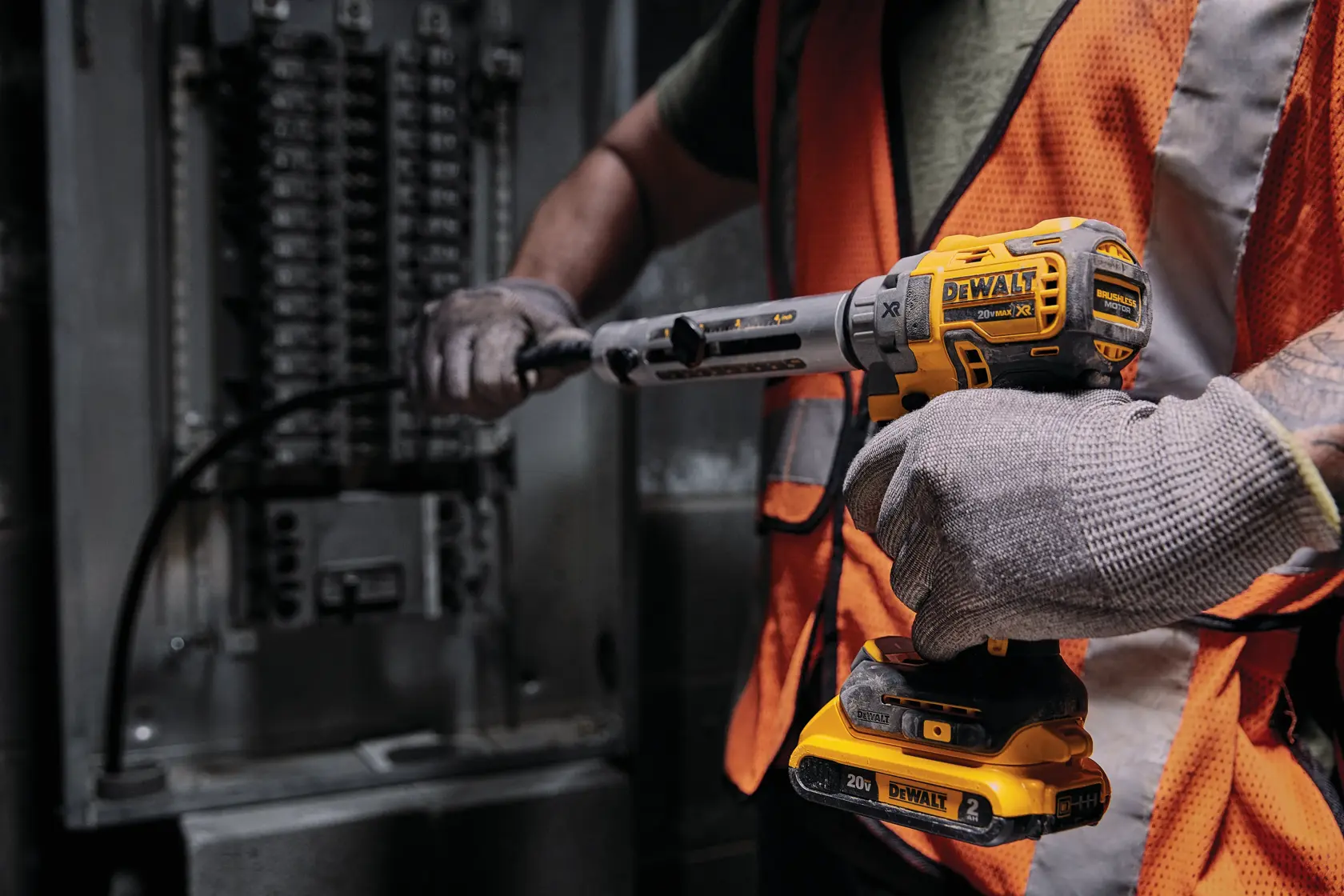 A person wearing gloves and an orange safety vest uses a DEWALT 20V cordless power tool to work on an electrical panel.